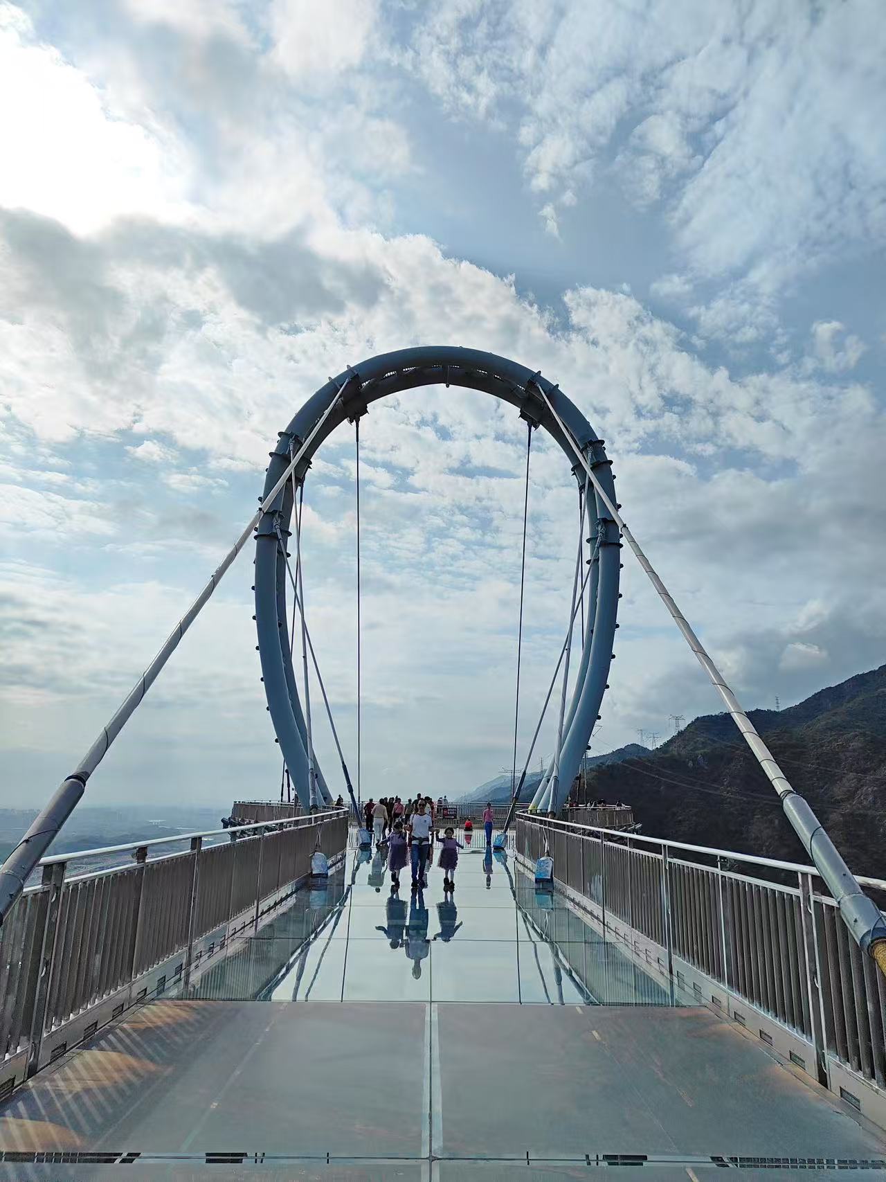 雲端漫步天門懸廊！全透明玻璃橋面倒映著藍天白雲，巨型鋼拱橫跨天際，遊客們漫步其上，腳下是 500 米高空峽谷，360° 全景視野，驚險又出片