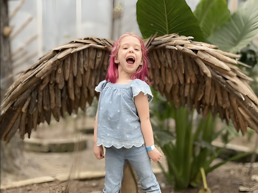 一個女孩在一組色彩鮮豔的假翅膀前高興地擺姿勢拍照,笑容燦爛 一個女孩在一組色彩鮮豔的假翅膀前高興地擺姿勢拍照,笑容燦爛