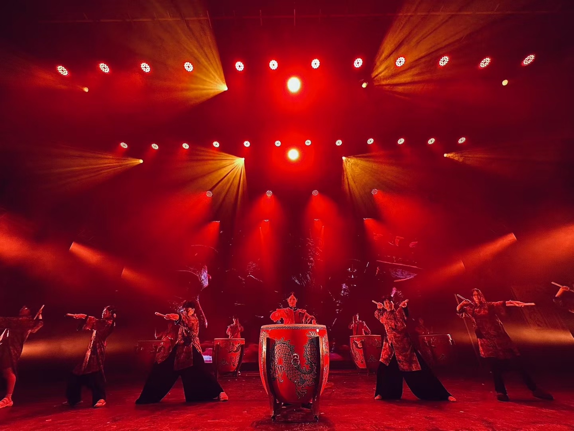 紅衣演員們於紅光射燈下擊鼓，龍紋鼓與剛勁動作相融，舞臺熱烈震撼