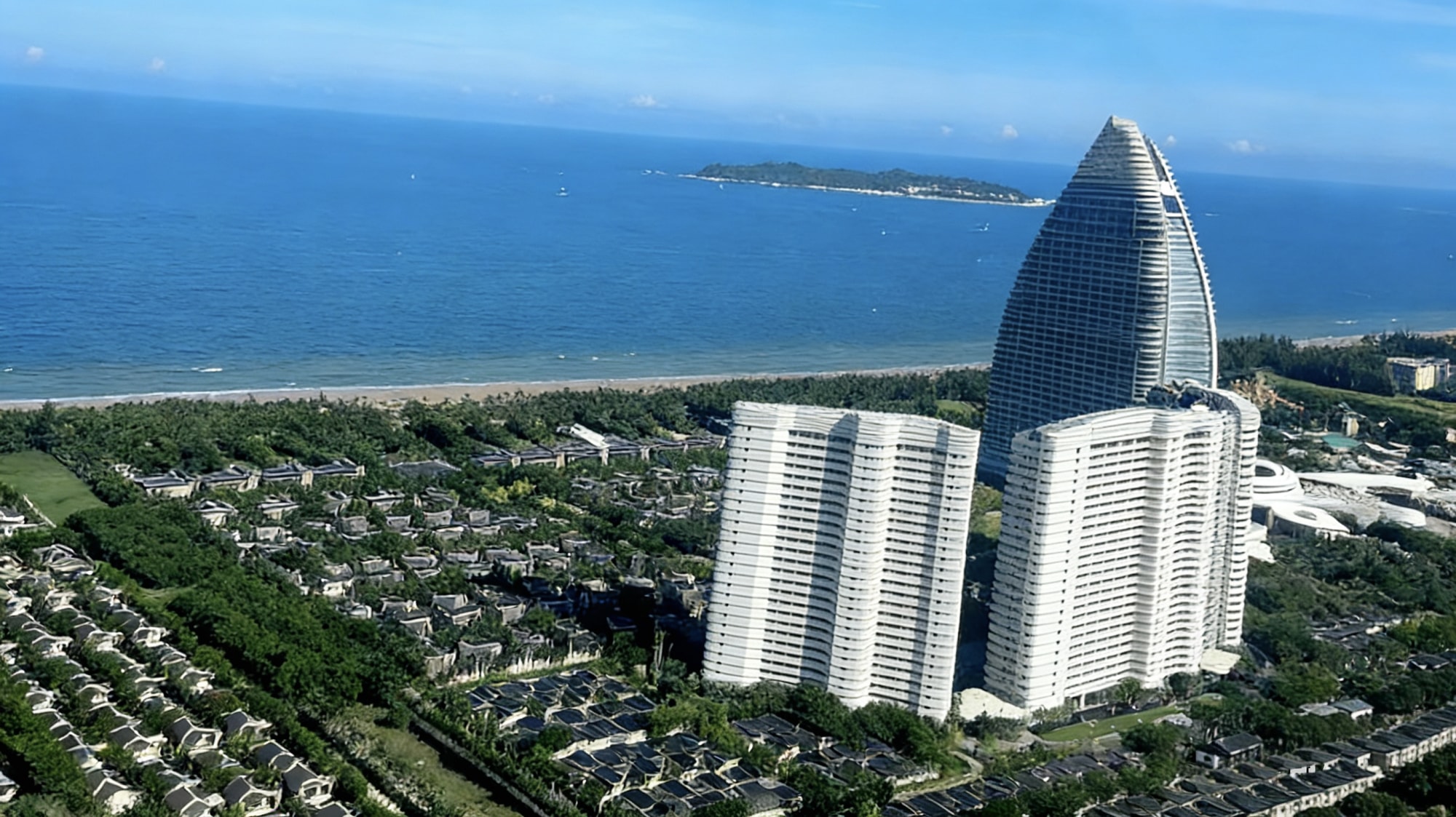 高樓群在椰林裡探出尖頂，遠處蜈支洲島像顆被藍綢裹著的綠珍珠