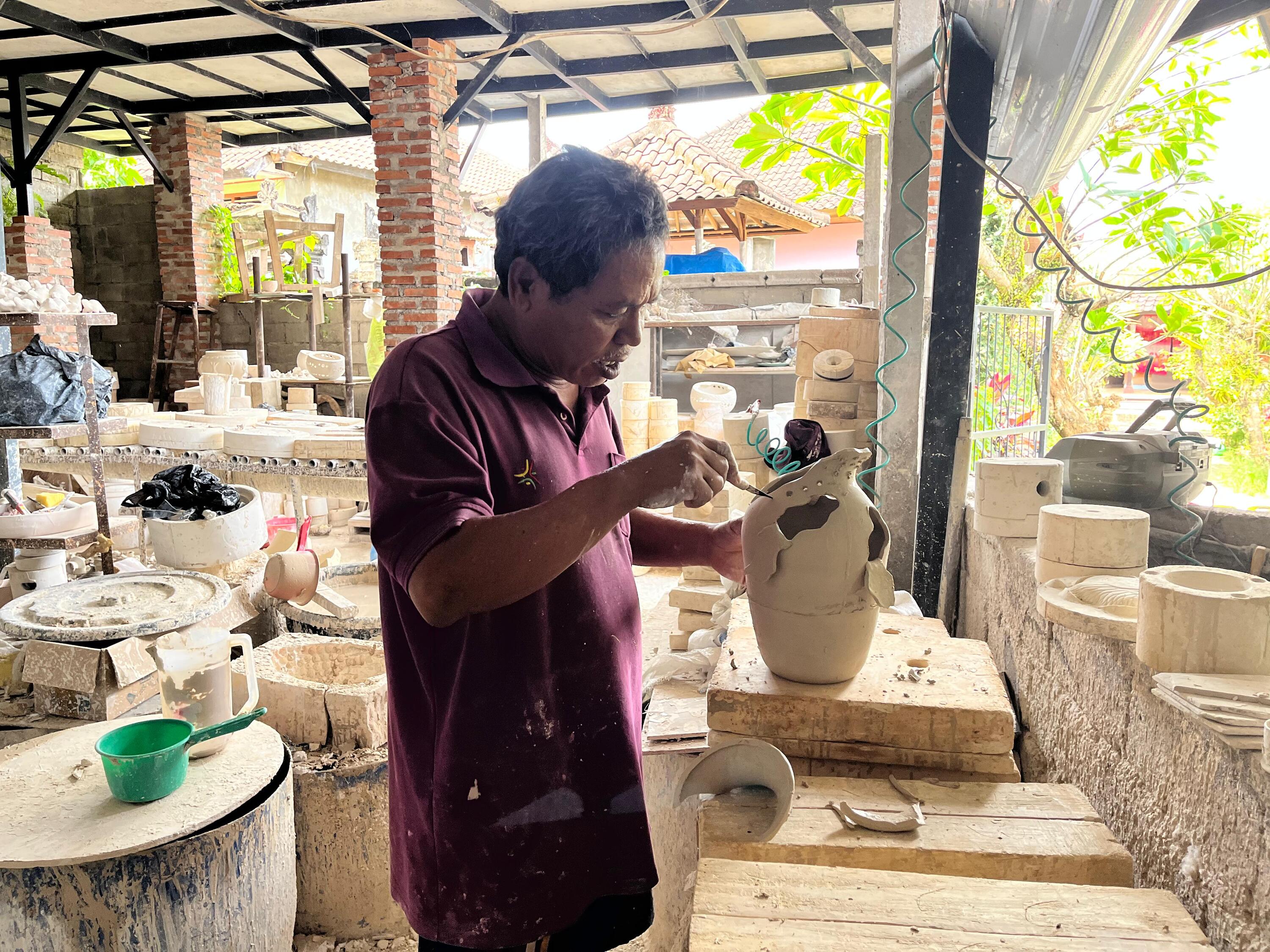 A skilled Balinese artist carefully shaping clay in the traditional ceramic studio.