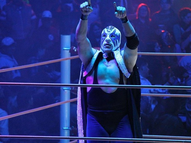 傳奇摔跤手在賽後自豪地擺姿勢，披風飄揚，粉絲們高呼著他標誌性的名字