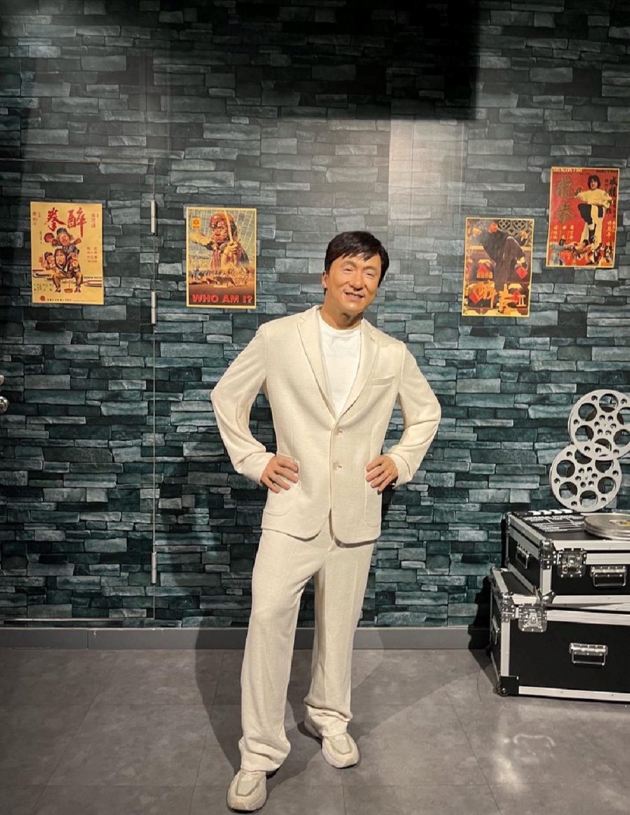 Jackie Chan wax figure, with his classic movie posters in the background, wearing a casual suit, showing Jackie Chan's iconic friendly attitude, paying tribute to this action movie star
