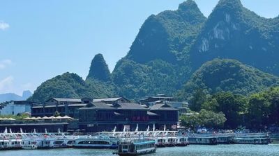 遊船碼頭停泊著多艘遊船，黛色建築與身後喀斯特峰林相映，是灕江遊的起點與歸處