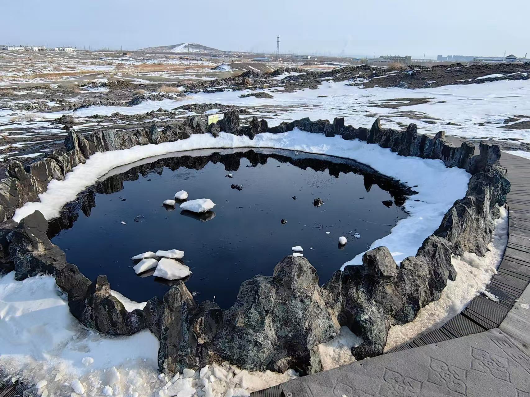 黑油山天然油池，黝黑油麵漂浮碎冰塊，四周黑石圍合，地面殘雪尚未消融。遠處曠野遼闊，油氣從地下自然滲出，這是獨有的地質奇觀，直觀感受這片土地天然原油溢出的神奇景象