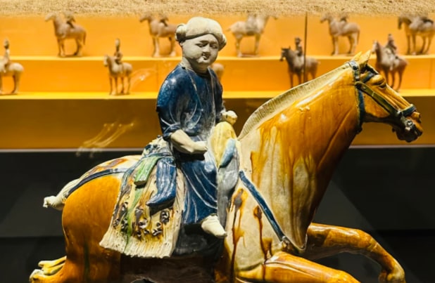 這是一件唐代的三彩騎馬俑,屬於陪葬用的陶製明器。它以黃、藍、白等典型的唐三彩釉色燒製而成,馬匹造型矯健有力,騎手神態安詳,服飾細節豐富,真實反映了唐代的社會風貌與出行禮儀。 這是一件唐代的三彩騎馬俑,屬於陪葬用的陶製明器。它以黃、藍、白等典型的唐三彩釉色燒製而成,馬匹造型矯健有力,騎手神態安詳,服飾細節豐富,真實反映了唐代的社會風貌與出行禮儀。