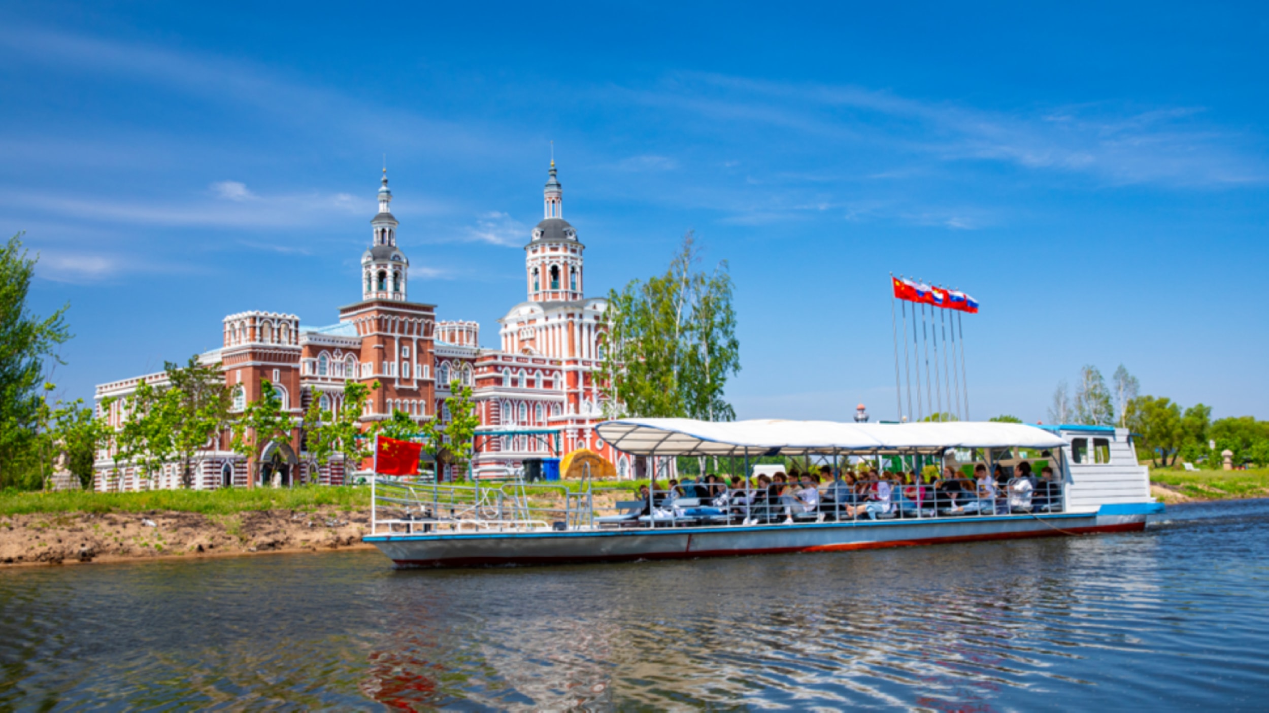 遊船載滿遊客,在水面行駛。岸邊是紅白色俄式建築,藍天綠樹映襯,景緻優美 遊船載滿遊客,在水面行駛。岸邊是紅白色俄式建築,藍天綠樹映襯,景緻優美