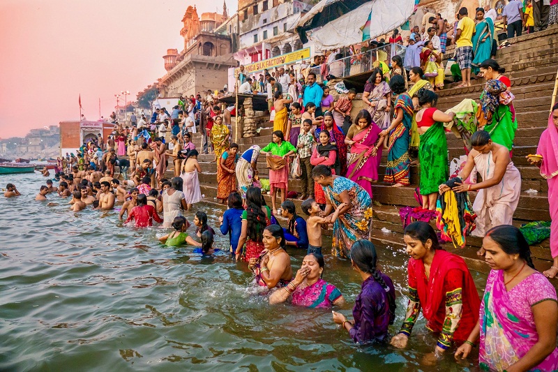 Showing the colorful traditional clothing and Hindu religious ritual of bathing in the Ganges River from the ancient ghats of Varanasi.