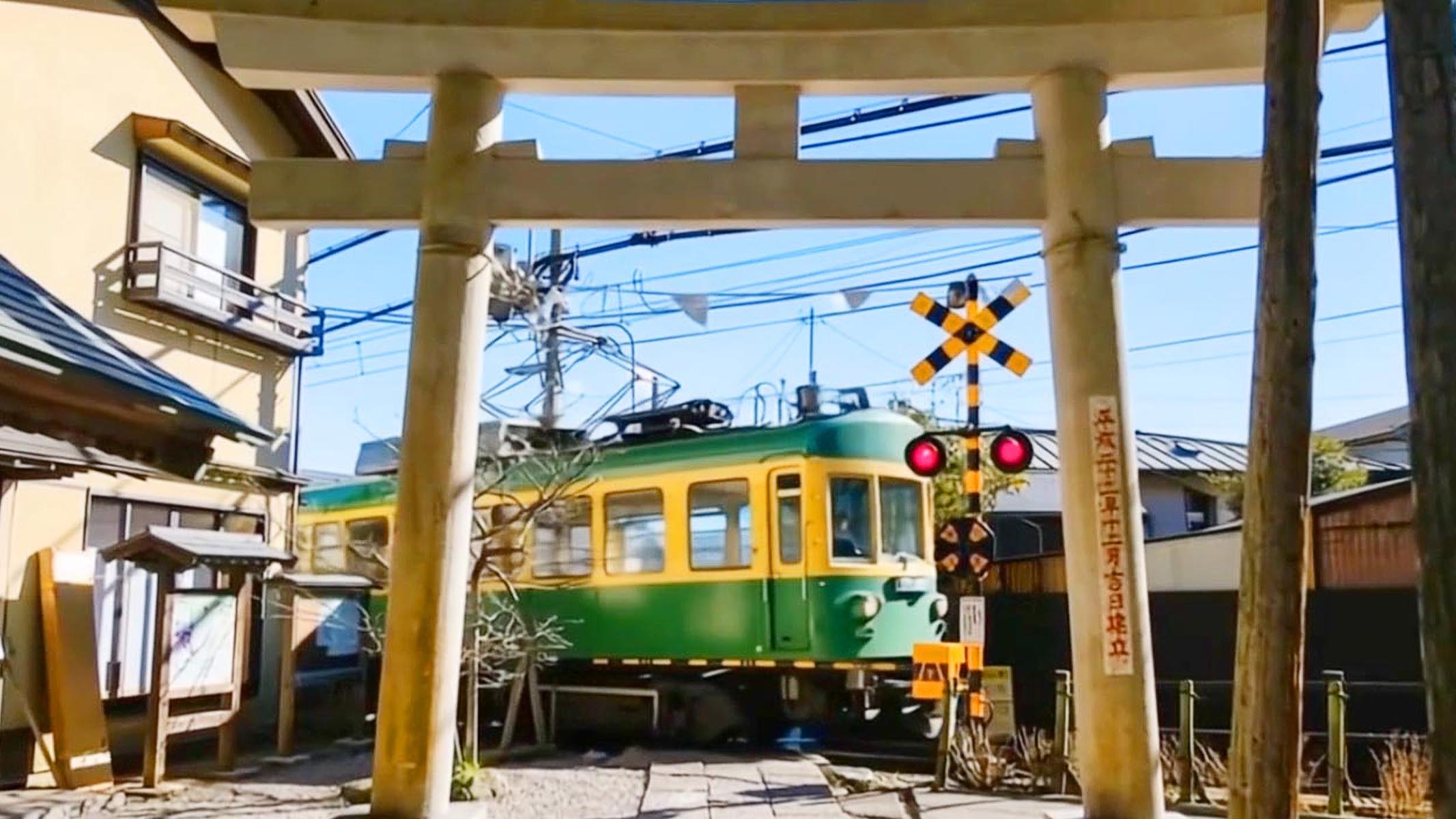 鳥居之下,江之電列車緩緩駛過,黃綠車身映襯藍天,鐵道與神社相鄰,街巷寧靜,展現鎌倉獨特風情 鳥居之下,江之電列車緩緩駛過,黃綠車身映襯藍天,鐵道與神社相鄰,街巷寧靜,展現鎌倉獨特風情