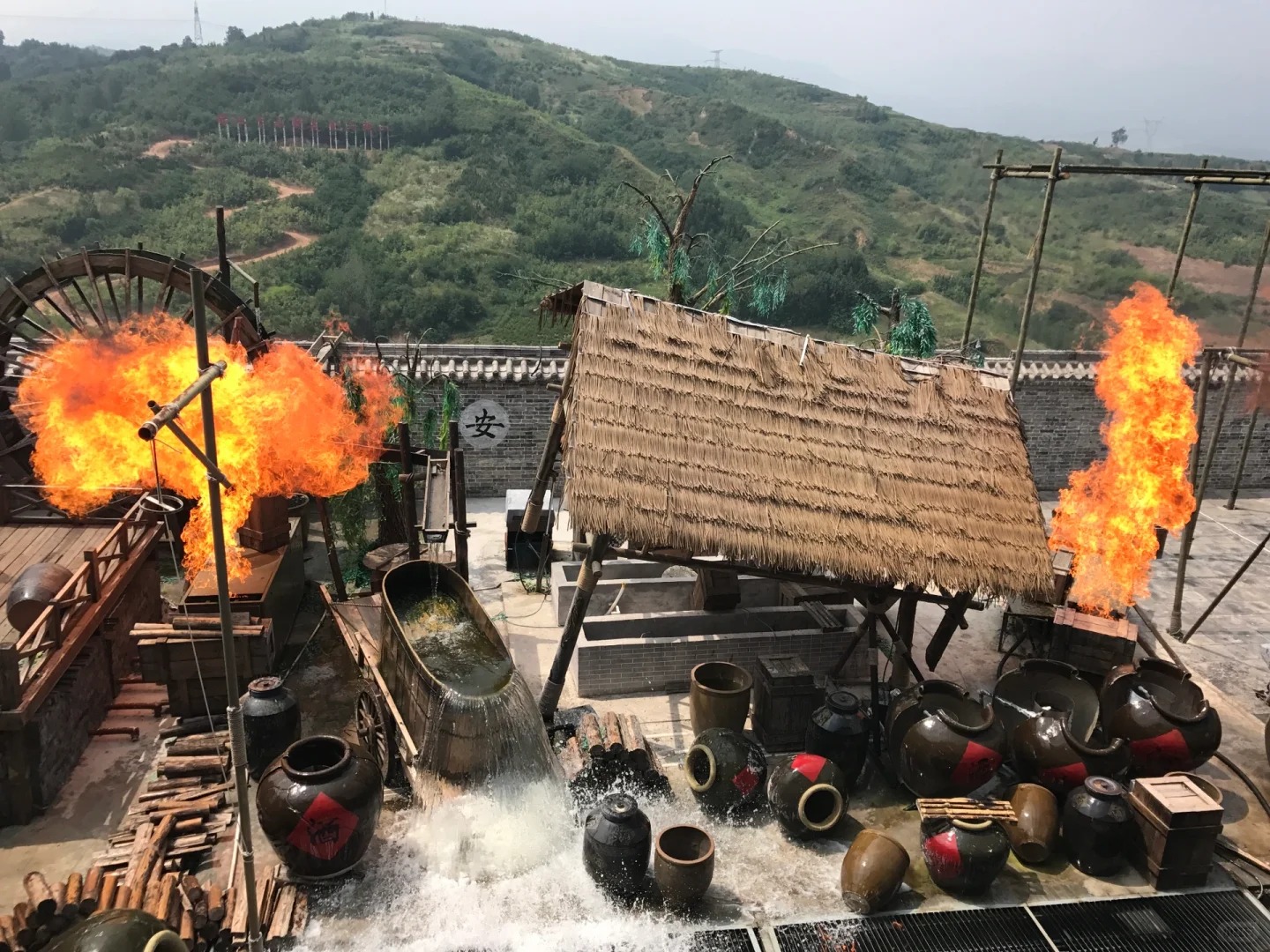 白鹿原影視城的實景演出場景,展現關中特色風貌:以茅草屋、大水車、酒罈等元素,還原傳統釀酒作坊,熊熊火焰增添緊張刺激感,配合山水背景,營造出沉浸式的視聽體驗 白鹿原影視城的實景演出場景,展現關中特色風貌:以茅草屋、大水車、酒罈等元素,還原傳統釀酒作坊,熊熊火焰增添緊張刺激感,配合山水背景,營造出沉浸式的視聽體驗