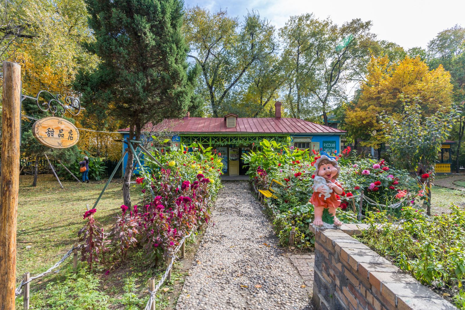 小花園中橘色鮮花盛開，一個戴藍帽子的可愛小矮人雕像立於花叢