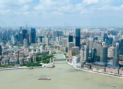 上海城市的高空俯瞰圖，黃浦江蜿蜒流淌，江面上有船隻航行，兩岸高樓密集，既有現代化的摩天大樓，也有具有歷史感的建築