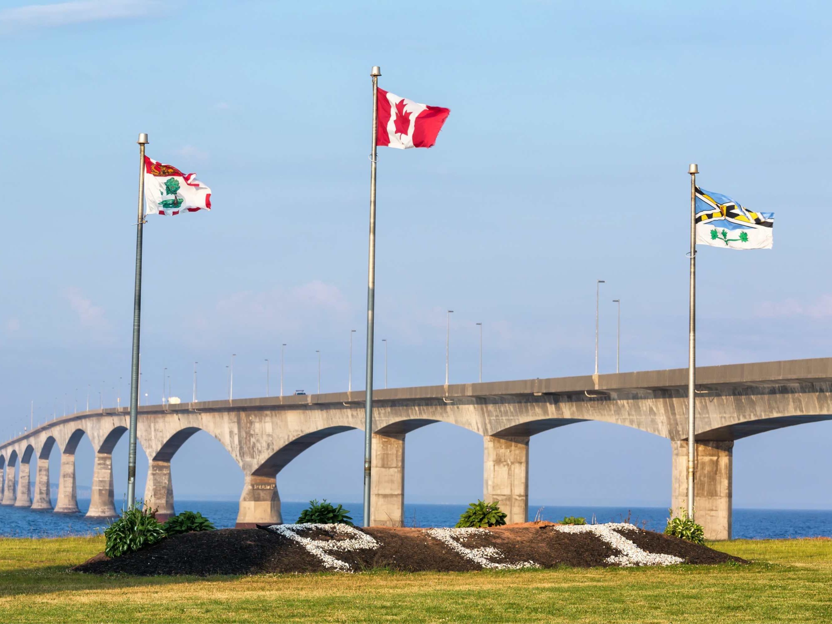 Visitors photographing a heritage building draped with Canadian flags celebrating Charlottetown’s national historical significance