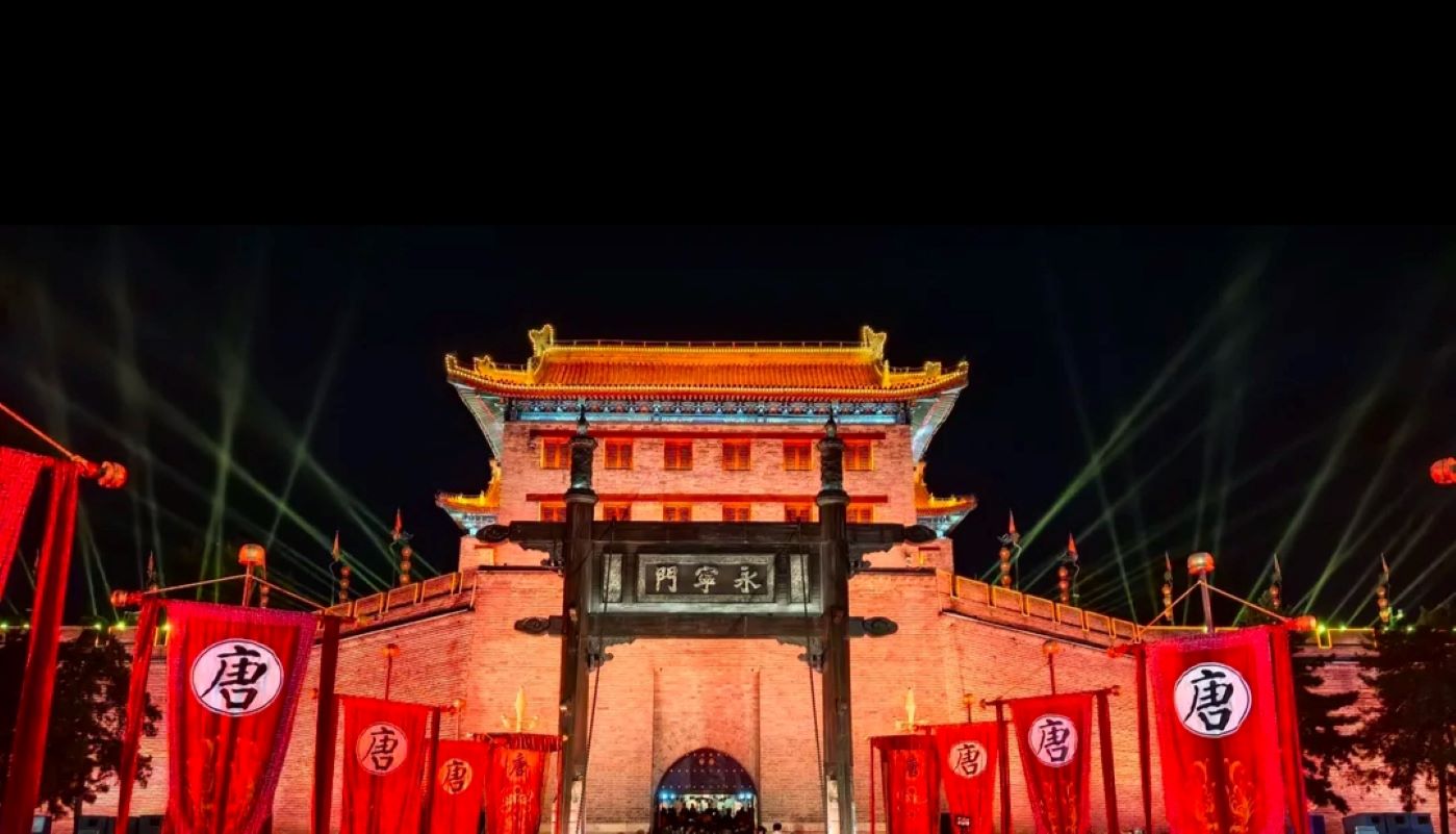巍峨的永寧門城樓在夜色中燈火輝煌，紅色的旗幟迎風飄揚，上面印有醒目的 “唐” 字