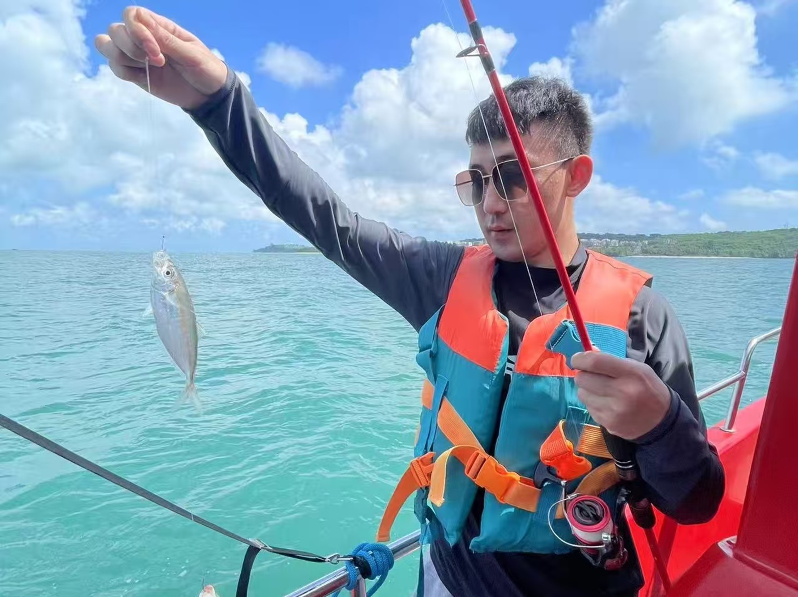 穿救生衣的人在船舷舉竿,釣線懸著小魚,藍海襯著晴空,是海釣初獲的輕快與愜意 穿救生衣的人在船舷舉竿,釣線懸著小魚,藍海襯著晴空,是海釣初獲的輕快與愜意