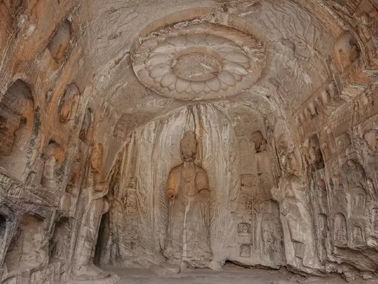 萬佛洞內部景象:穹頂刻有精美蓮花藻井,中央主尊佛像衣袂飄逸,四周巖壁密佈千佛小龕,石刻線條細膩繁複,展現了唐代石窟藝術的精緻與繁複 萬佛洞內部景象:穹頂刻有精美蓮花藻井,中央主尊佛像衣袂飄逸,四周巖壁密佈千佛小龕,石刻線條細膩繁複,展現了唐代石窟藝術的精緻與繁複