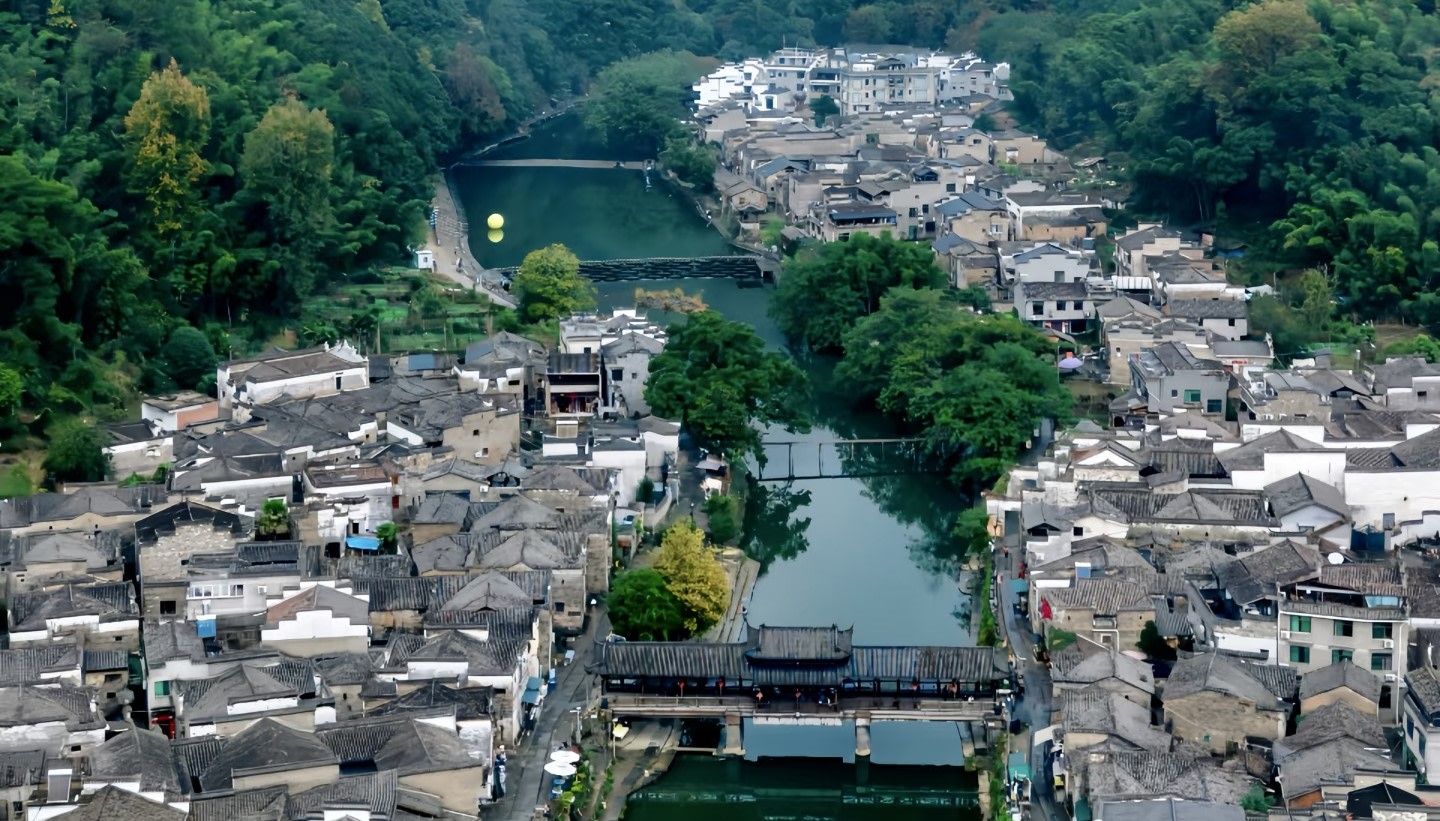 從高空俯瞰，古村如一塊被河水溫柔環抱的璞玉，白牆黛瓦的屋舍沿河岸鋪展，廊橋、石墩橋與木橋橫跨水面