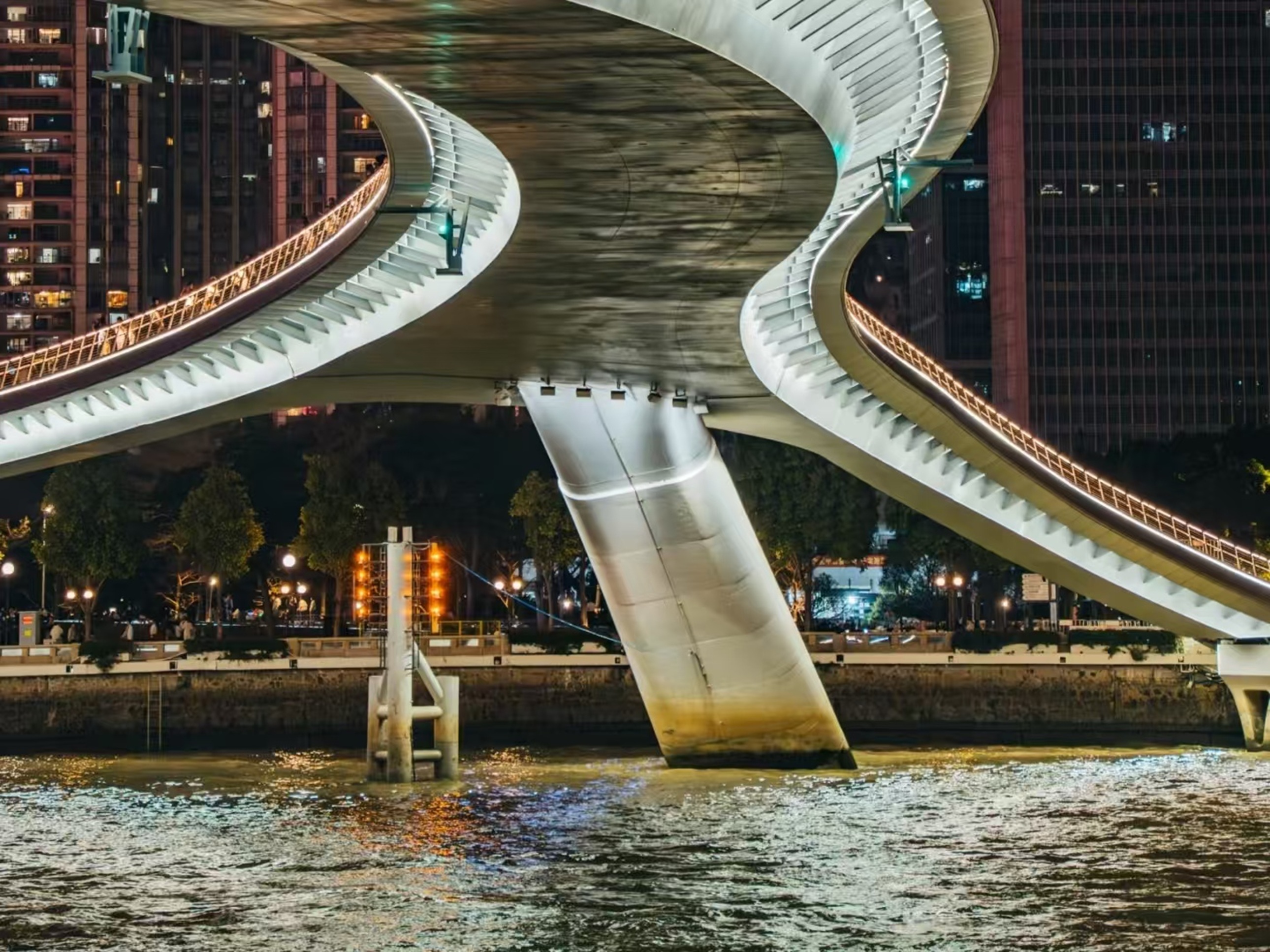 螺旋式橋身搭配燈帶,橋下立柱浸於江水中,岸邊燈光與橋面行人剪影相融,盡顯建築美學與夜間菸火氣 螺旋式橋身搭配燈帶,橋下立柱浸於江水中,岸邊燈光與橋面行人剪影相融,盡顯建築美學與夜間菸火氣