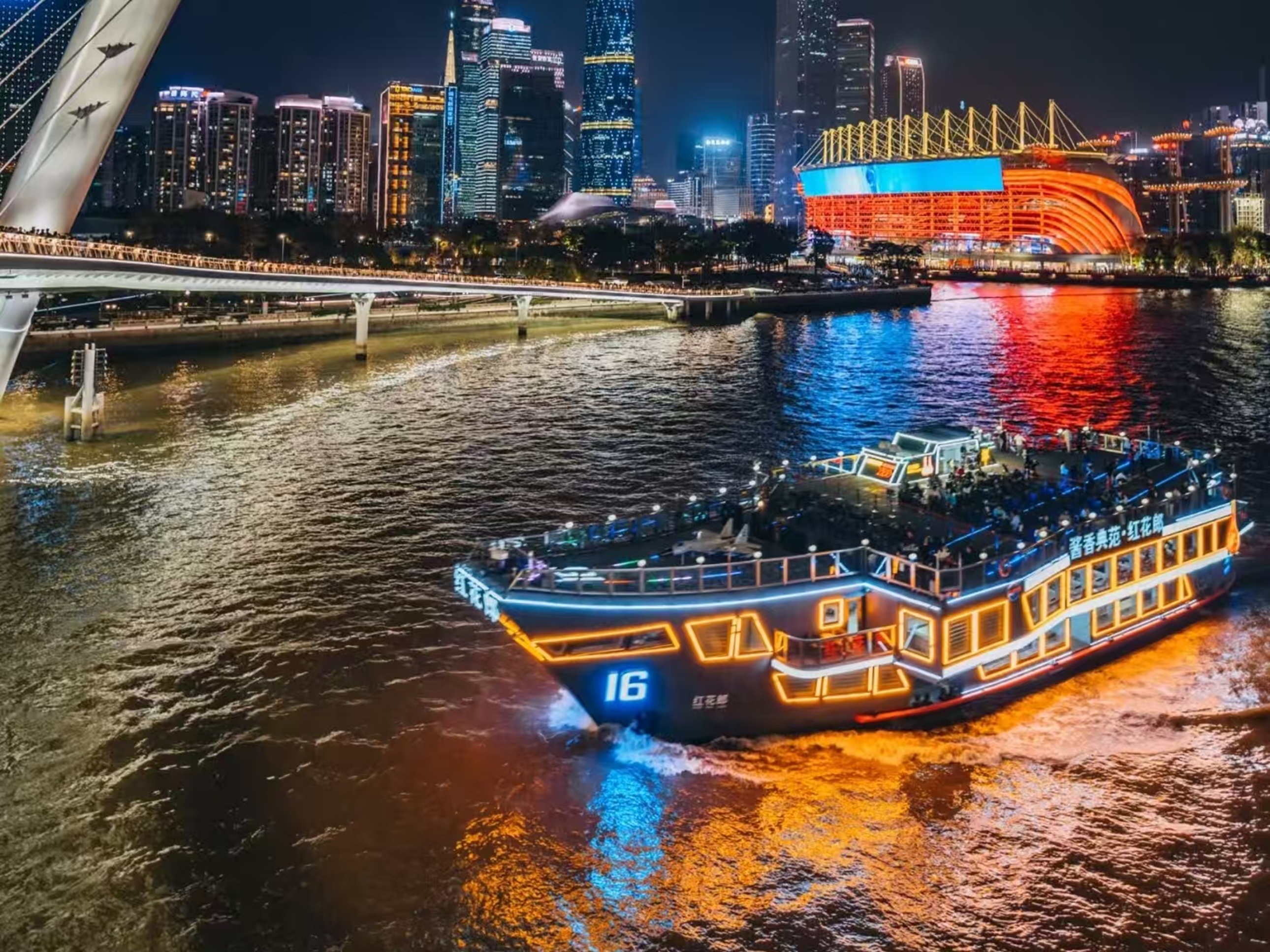 船身飾以暖黃燈光,甲板遊客簇擁觀景,背景海心橋與亞運場館燈光交織,江風裡盡是廣州夜生活的熱鬧 船身飾以暖黃燈光,甲板遊客簇擁觀景,背景海心橋與亞運場館燈光交織,江風裡盡是廣州夜生活的熱鬧