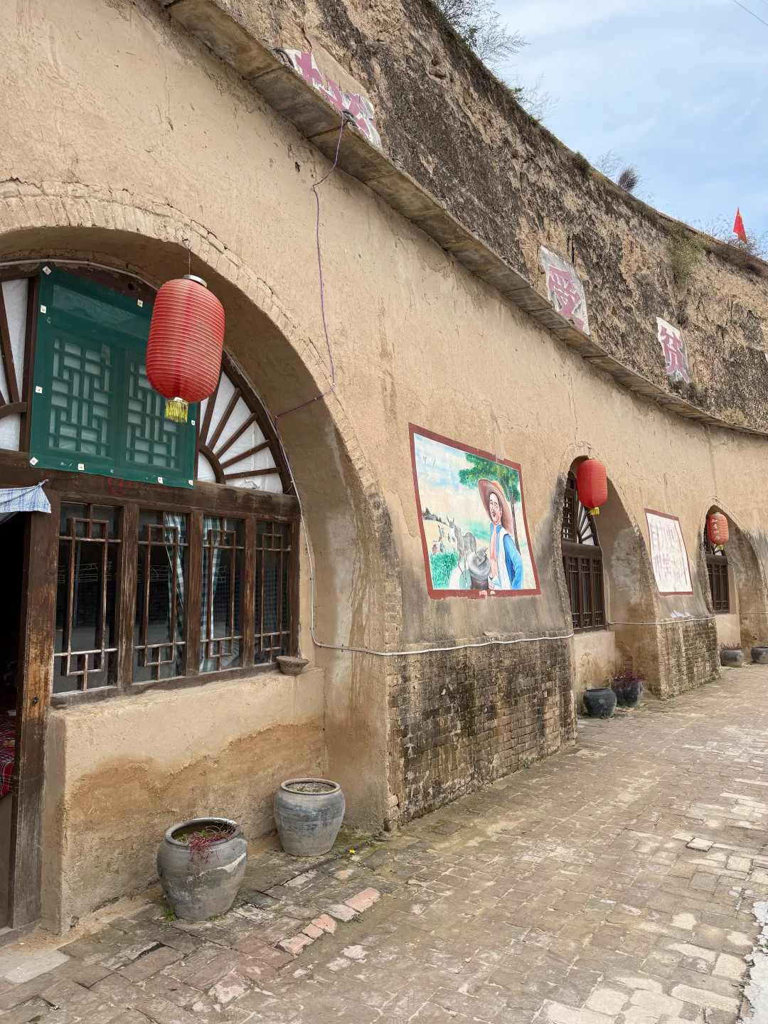 黃土夯築的老式窯洞院落，拱形土窯洞古樸厚重，木格窗欞搭配紅燈籠，牆面留存懷舊彩繪，土坯磚牆、老陶甕盡顯濃郁的西北鄉土歲月氣息