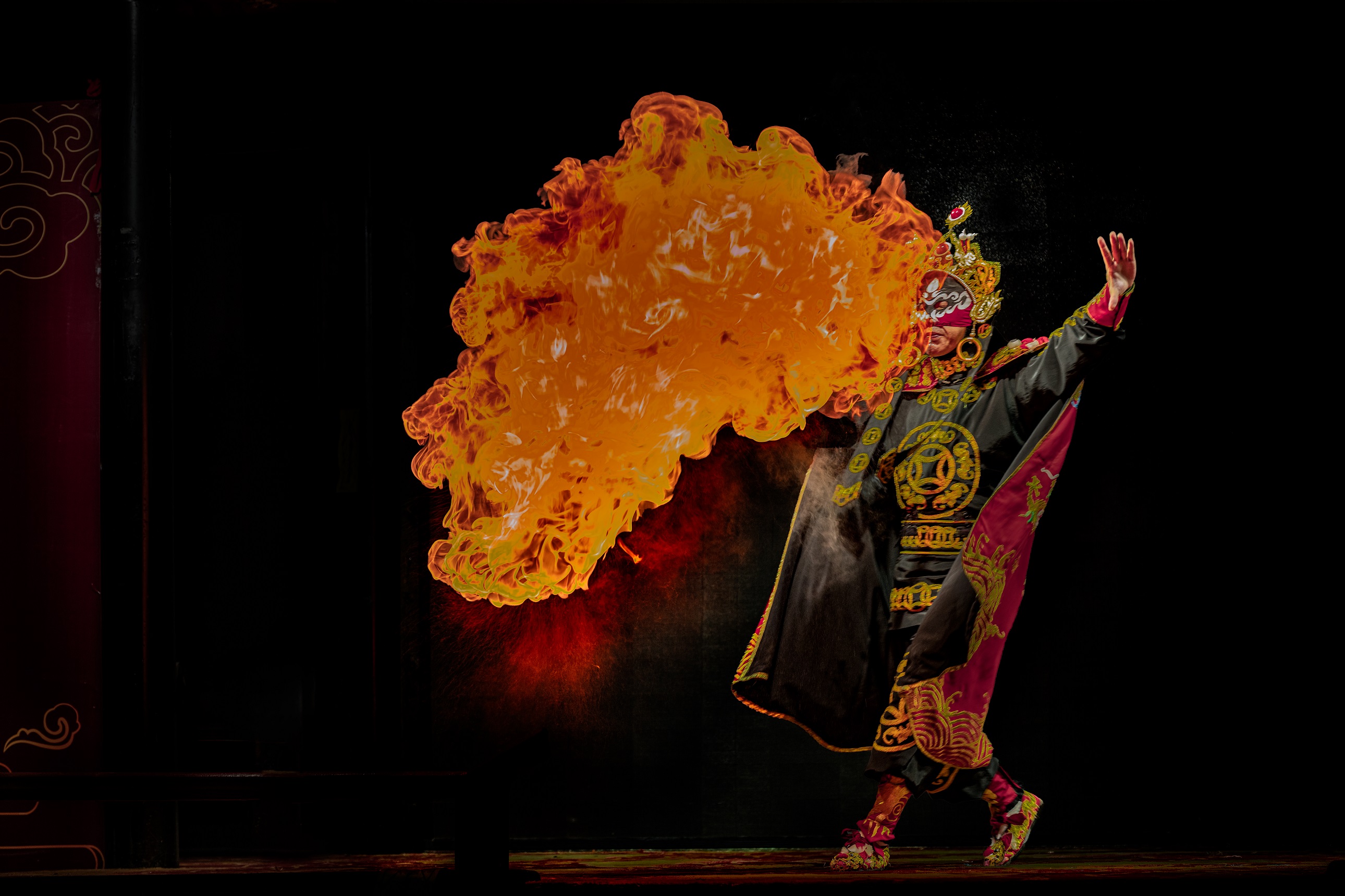 變臉演員身著裝飾華麗的戲服，頭戴精緻盔頭，正表演噴火絕技，巨大的火焰在他身側騰起，在黑色背景的襯托下，場面極具視覺衝擊力，盡顯川劇絕活的神奇魅力