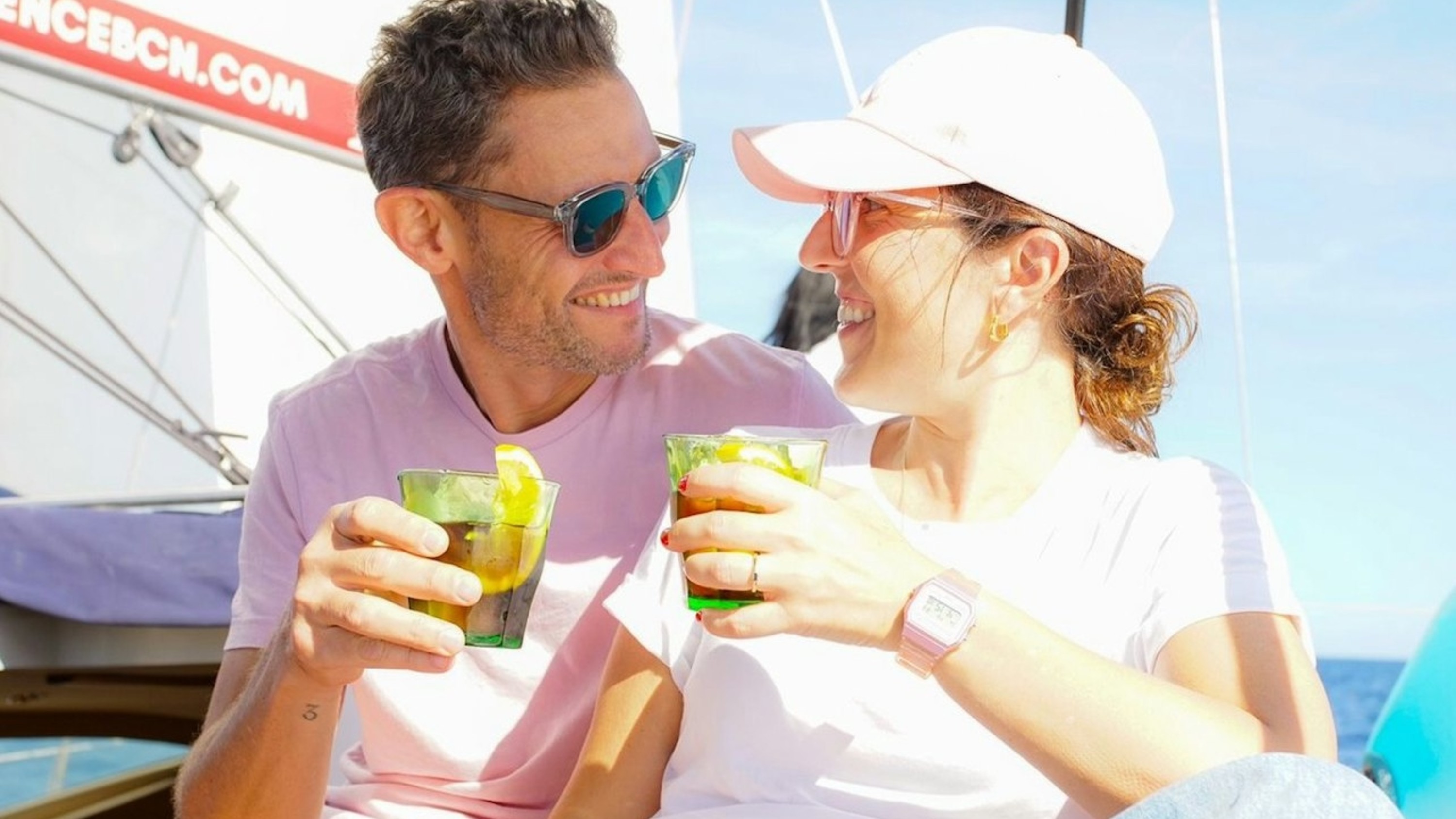 A couple exchanging warm smiles, each holding a drink under golden sunlight and breeze