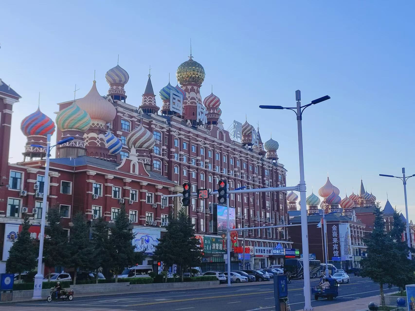 畫面展現充滿俄式風情的城市街景，紅調主體建築搭配五彩斑斕的洋蔥頭穹頂，造型華麗別緻。街道上車流往來，路燈商鋪林立，澄澈藍天映襯異域樓宇，濃郁的邊境城市風貌撲面而來