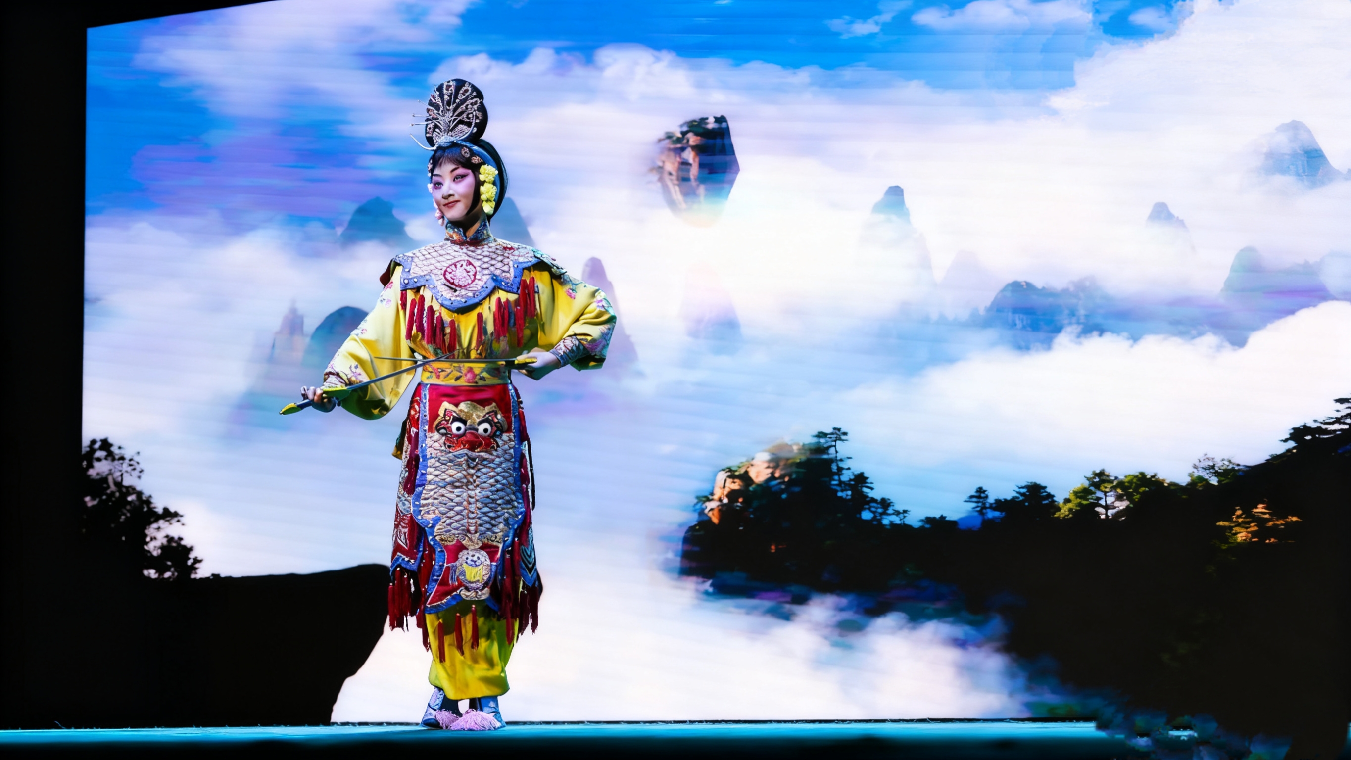 武旦演員身著黃色戲服,手持兵器,姿態英武。背景是雲霧繚繞的山水佈景,演員的每一個動作都充滿力量感,展現出了一位女中豪傑的颯爽英姿,將京劇武旦的魅力展現得淋漓盡致 武旦演員身著黃色戲服,手持兵器,姿態英武。背景是雲霧繚繞的山水佈景,演員的每一個動作都充滿力量感,展現出了一位女中豪傑的颯爽英姿,將京劇武旦的魅力展現得淋漓盡致