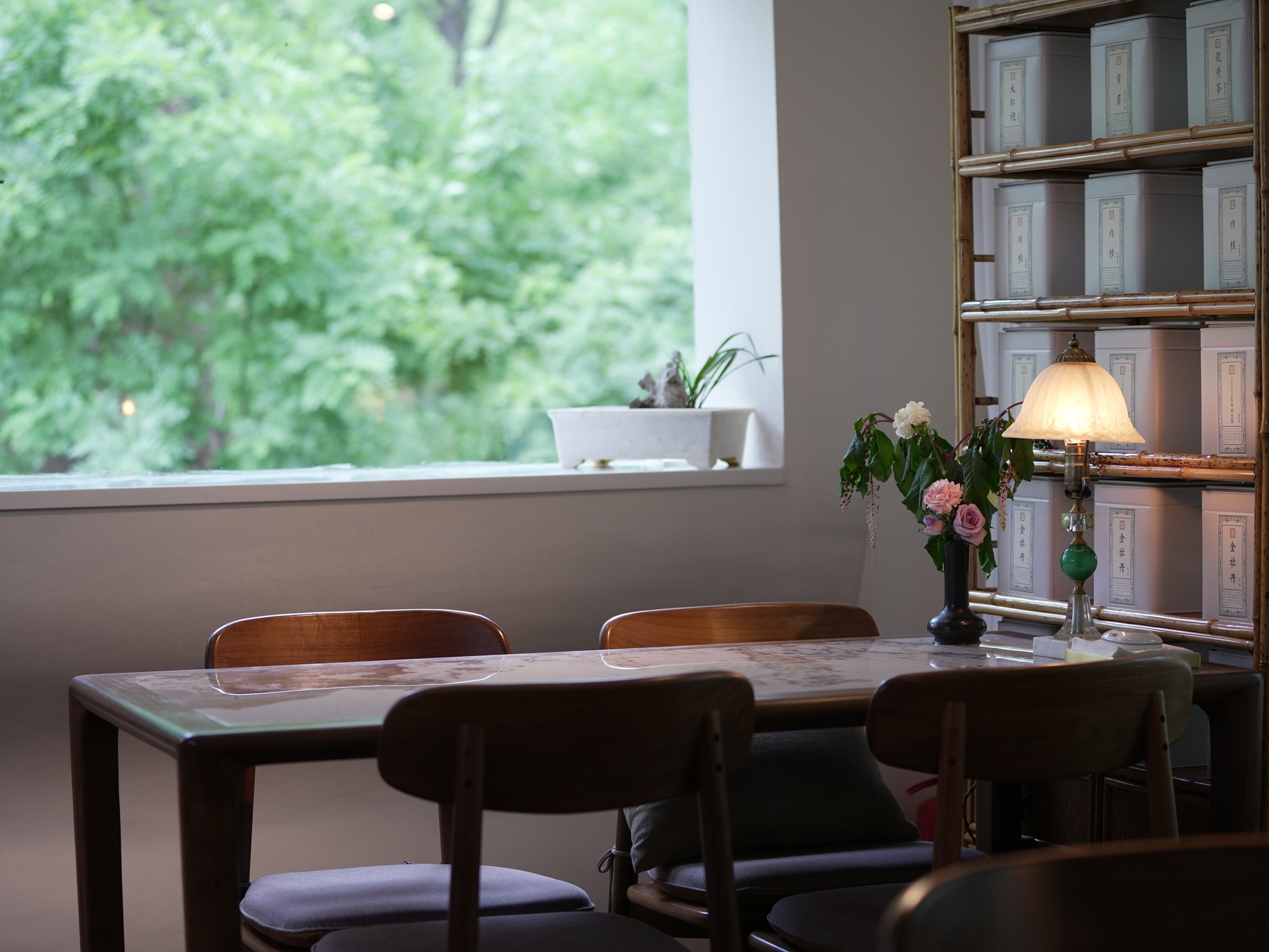 茶舍窗邊雅座，窗外綠意盎然，桌上燈與花，營造悠然品茶氛圍