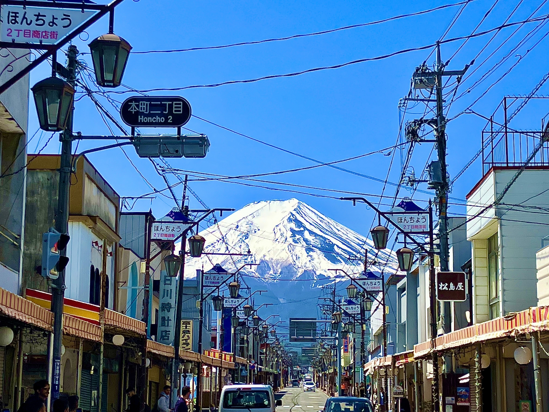 富士吉田市的本町商店街，是近年來極具人氣的富士山拍照景點。筆直延伸的街道兩側排列著復古商店與路燈，視線盡頭正好對準雄偉的富士山，形成極具震撼力的街景構圖。