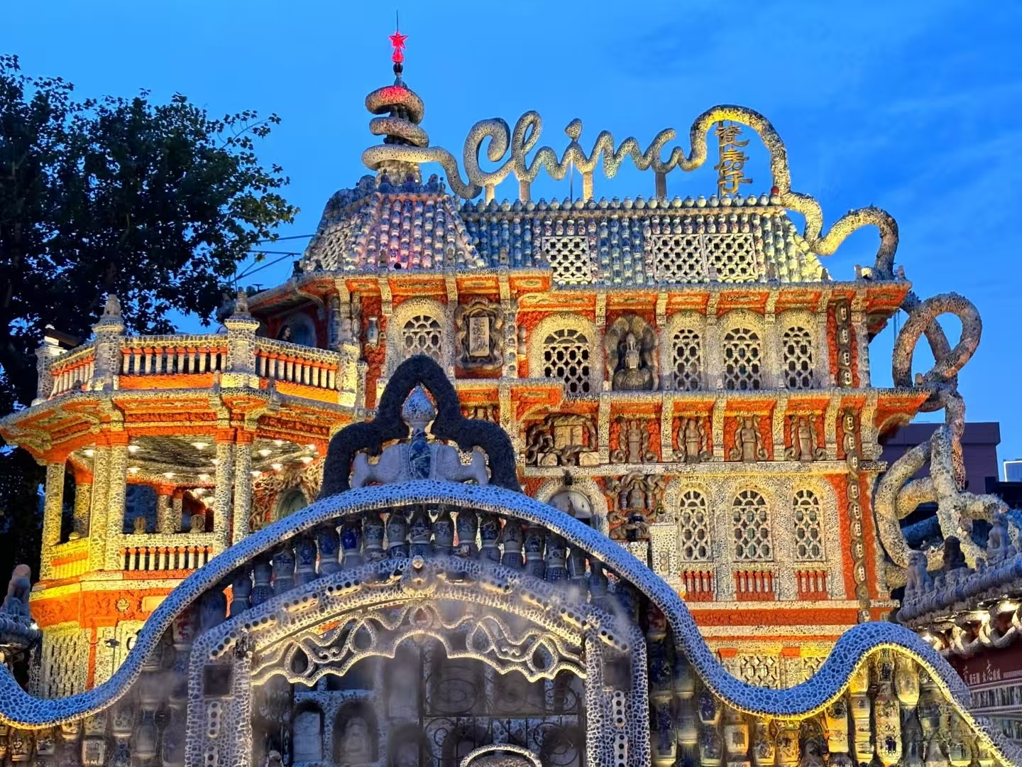 天津瓷房子在暮色中流光溢彩，整棟建築由瓷片、瓷瓶拼接而成，“China” 字樣醒目，前方瓷質拱門蜿蜒，盡顯中西合璧的藝術張力