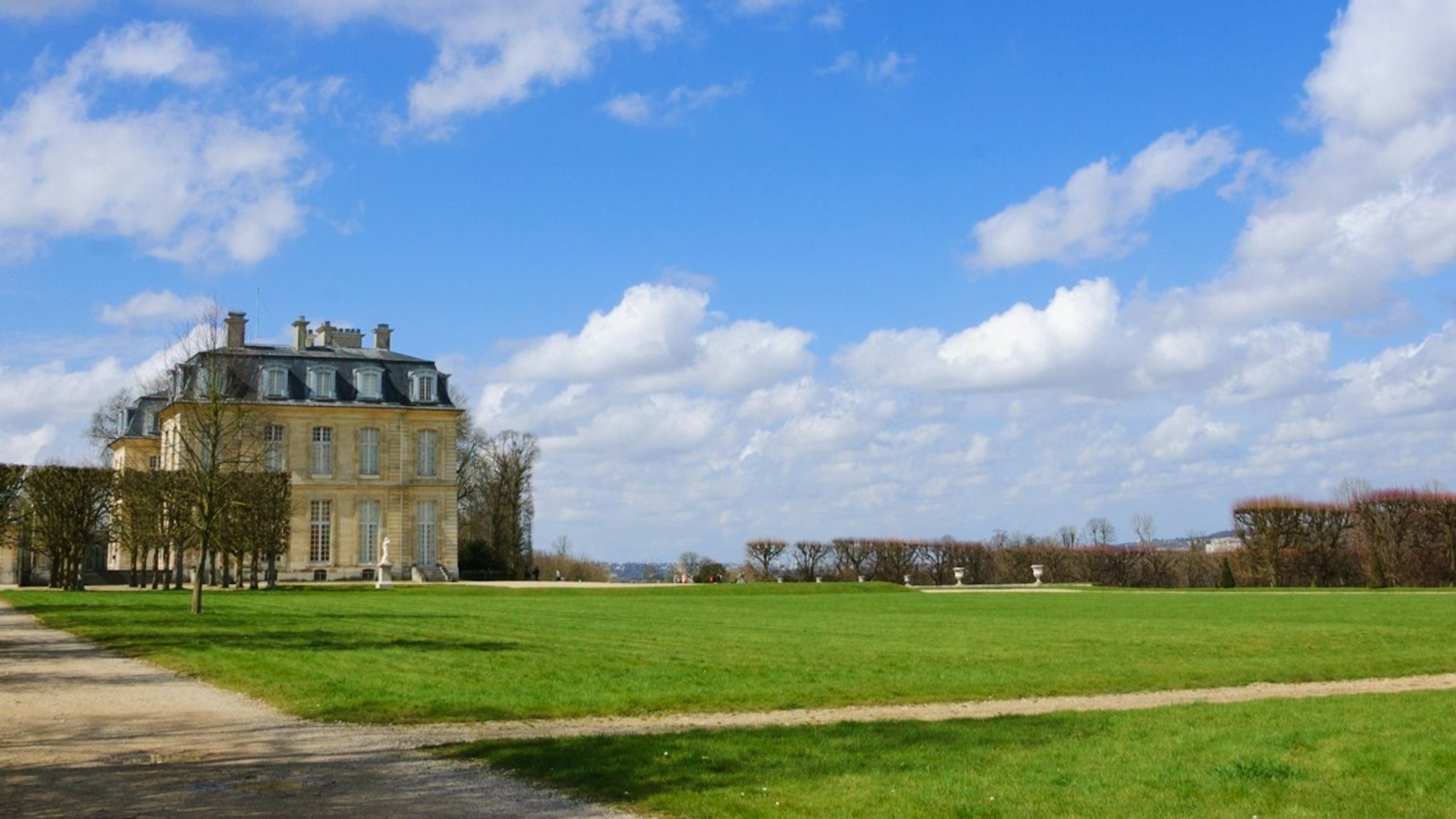 Grand chateau stands tall beyond a vast green lawn under clear blue sky