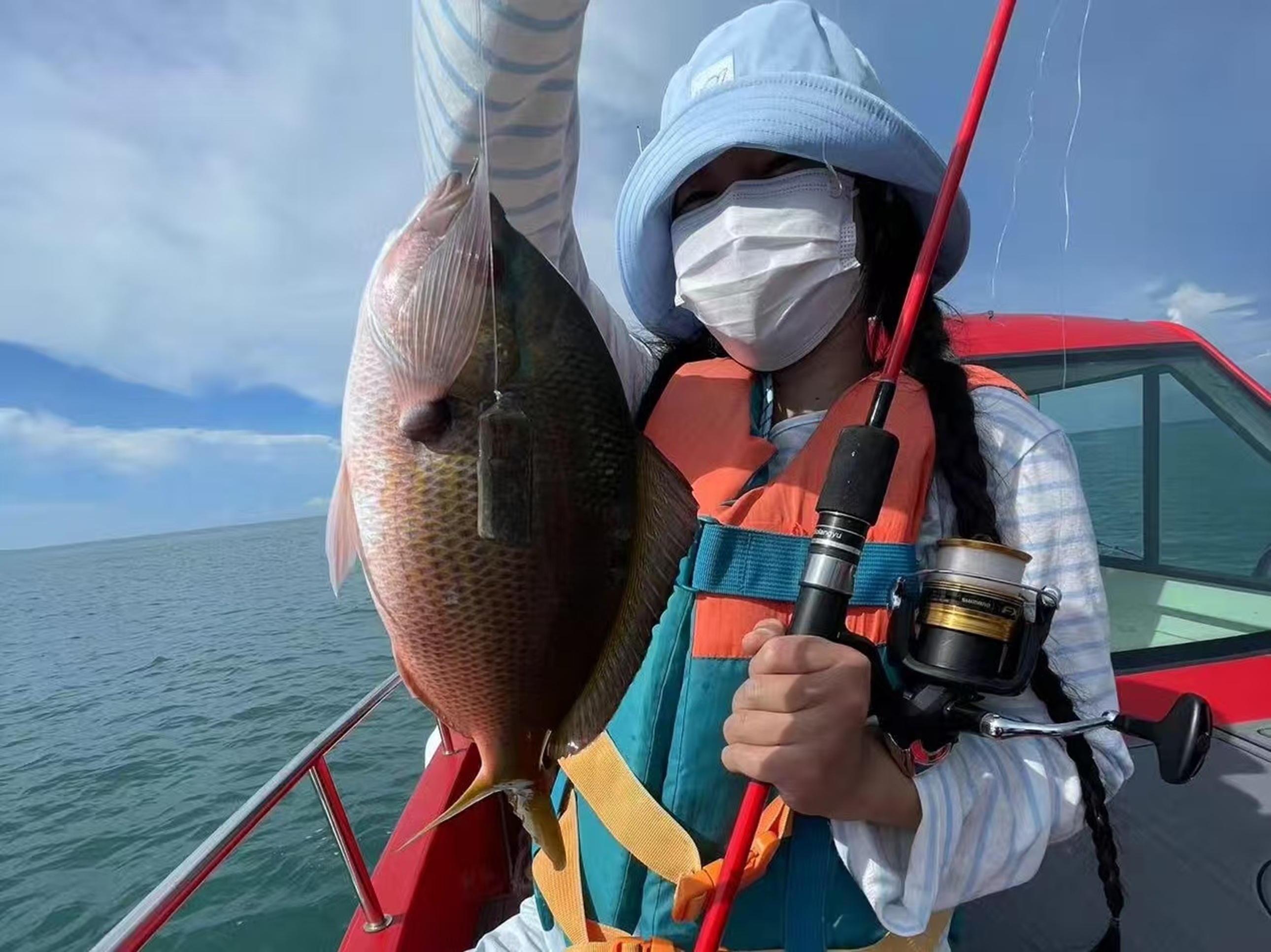 戴帽遮面的人持竿,釣線掛著肥碩的魚,紅船與藍海作景,是海釣收穫大魚的欣喜與滿足 戴帽遮面的人持竿,釣線掛著肥碩的魚,紅船與藍海作景,是海釣收穫大魚的欣喜與滿足