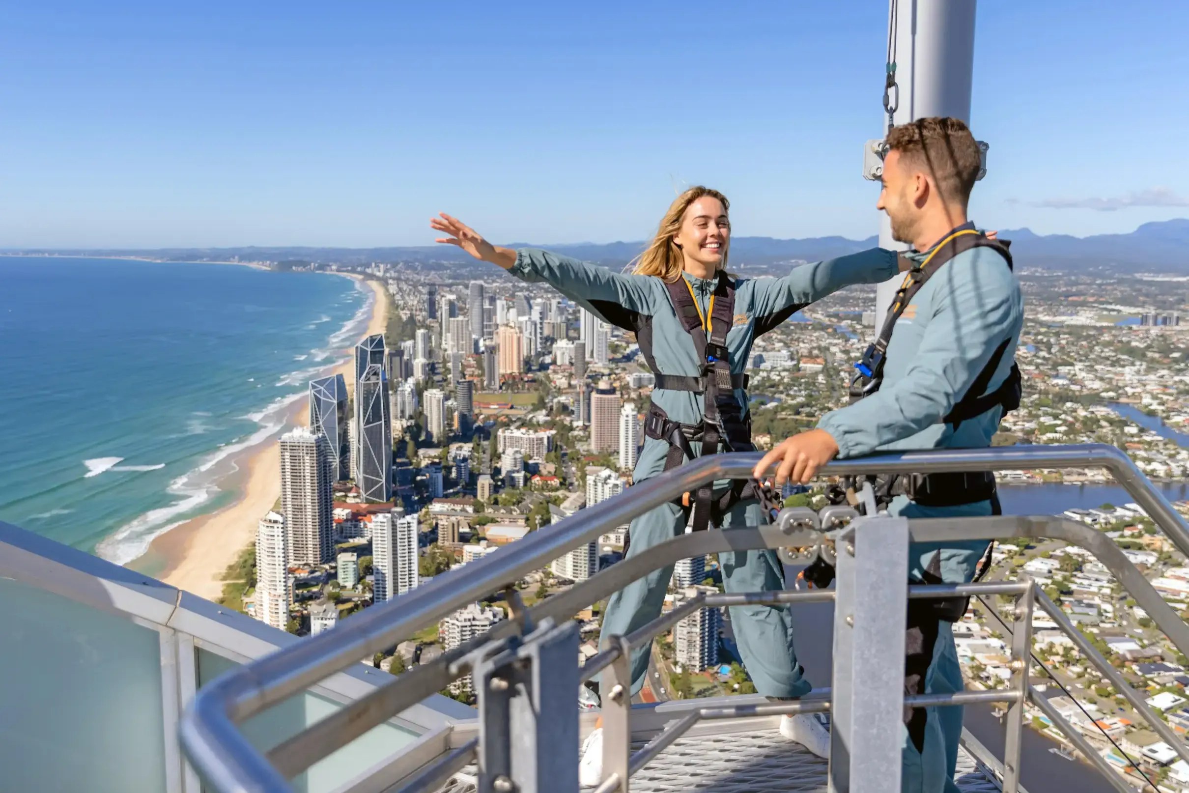 觀看兩位旅客在 SkyPoint 觀景台，於充滿活力的海岸景觀上方，分享這驚險刺激的攀登時刻。