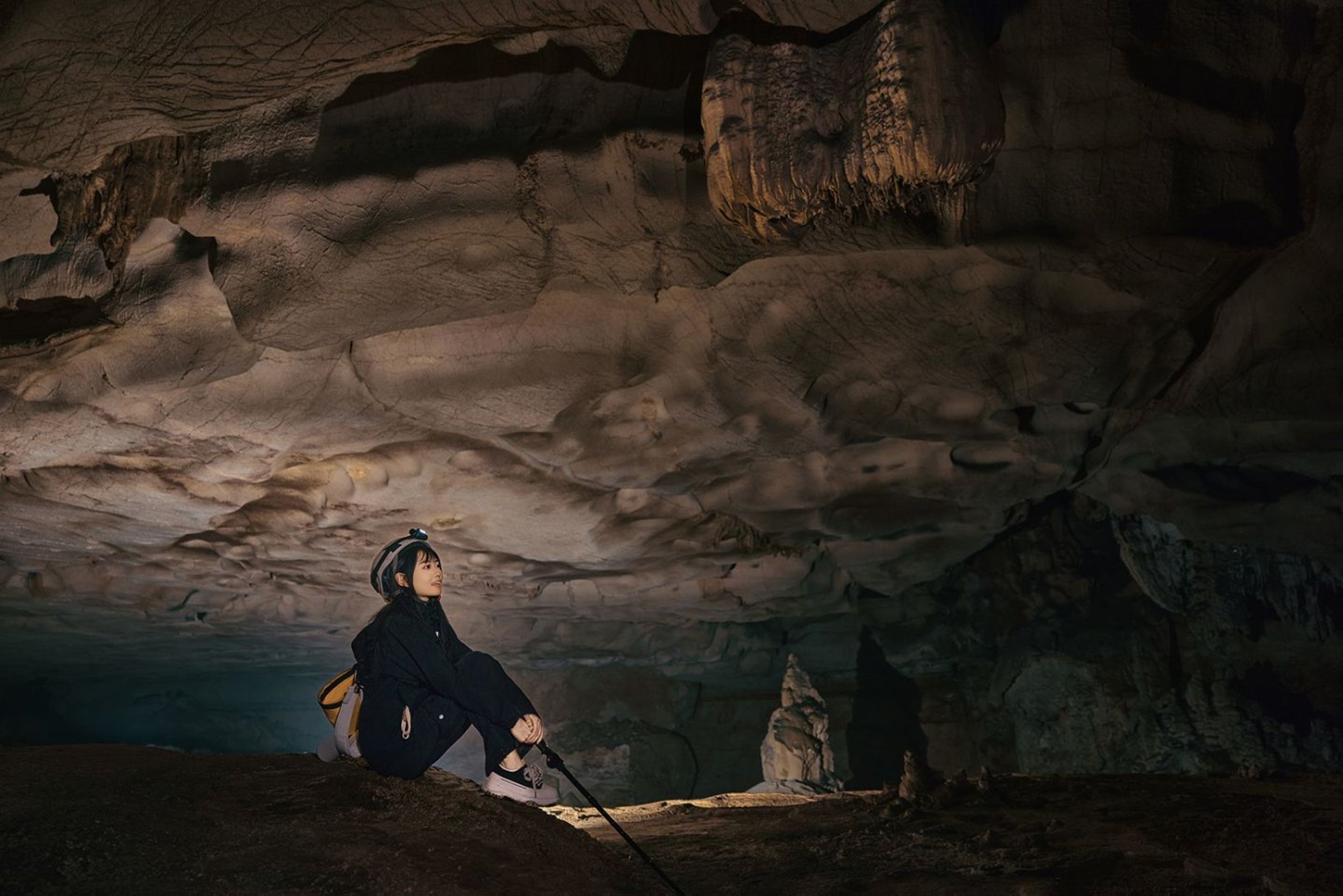 女孩坐在溶洞巖壁下,抬頭望向層疊的鐘乳石穹頂,暖光勾勒出巖壁紋理,身旁登山杖相伴,是探險途中的靜謐時刻 女孩坐在溶洞巖壁下,抬頭望向層疊的鐘乳石穹頂,暖光勾勒出巖壁紋理,身旁登山杖相伴,是探險途中的靜謐時刻