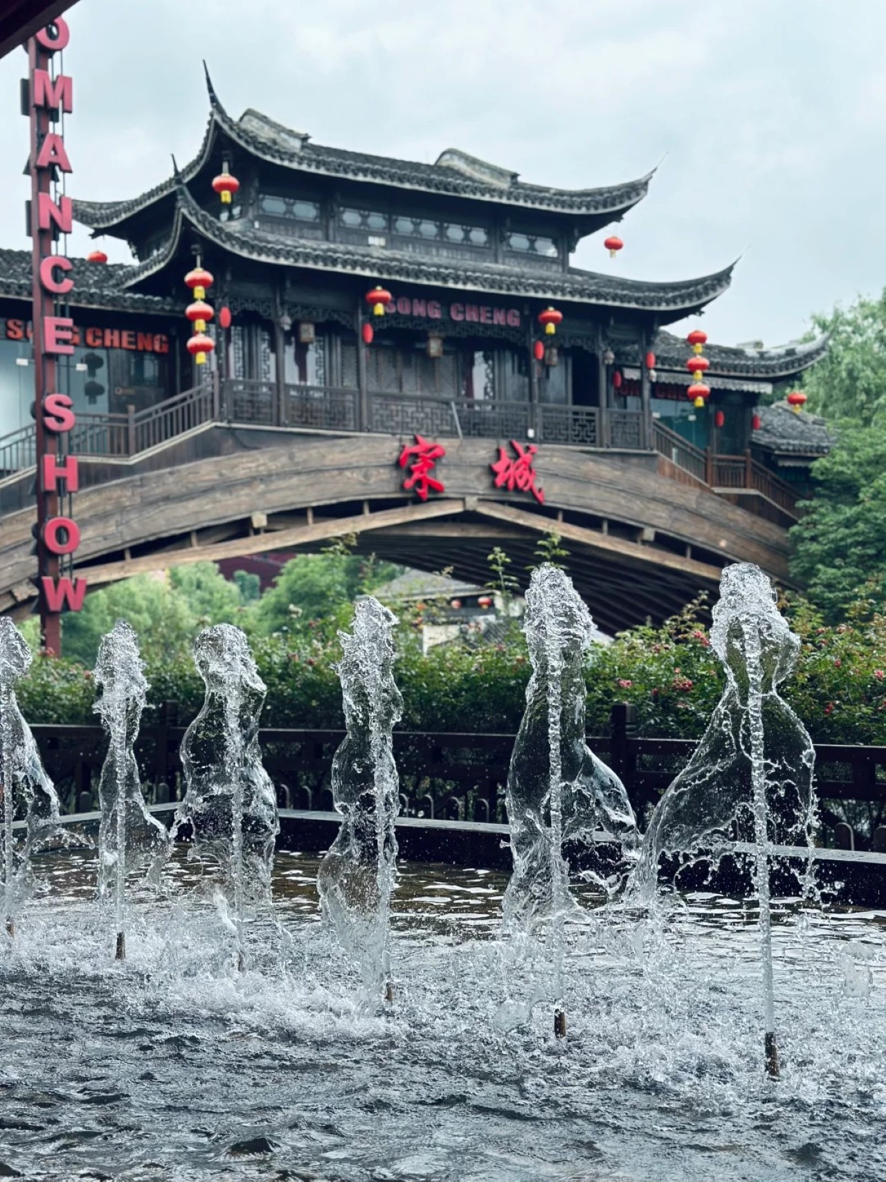 杭州宋城的一處場景。畫面中，古樸典雅的木質拱橋橫跨，橋上是典型的中式傳統建築，翹角飛簷，古色古香