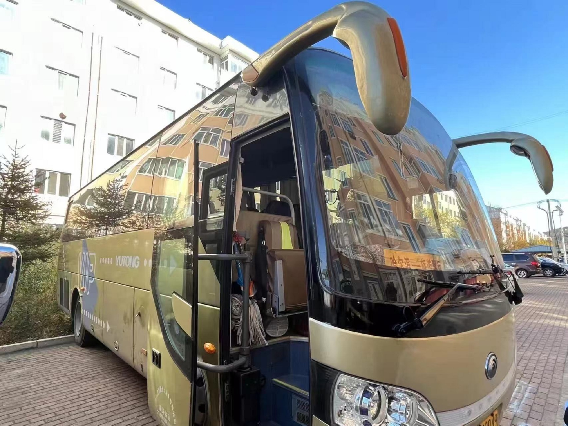 金色宇通大型旅遊大巴，車門處於開啟狀態，可看見車內座椅，擋風玻璃放置線路提示牌。車身漆面光亮，空間寬敞，行李艙可存放大件冰雪出行裝備，用於雪鄉、長白山區域之間的遊客轉運