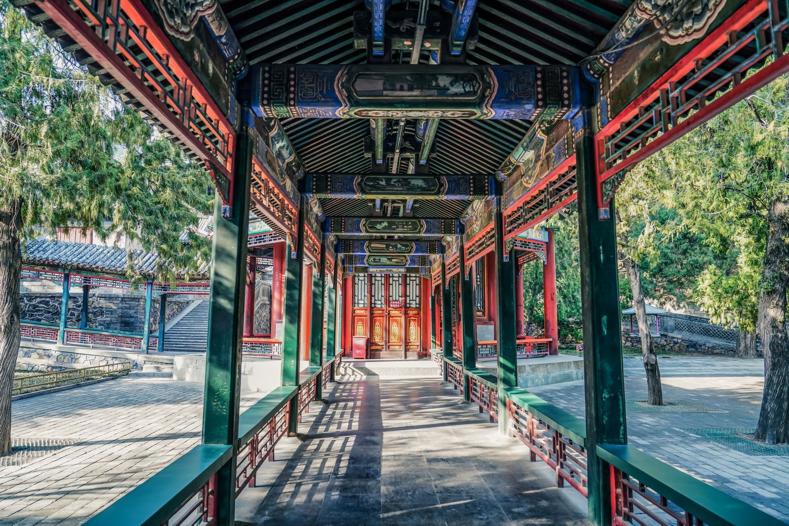 頤和園彩繪長廊縱深延伸，綠漆立柱與梁枋間的藍綠彩繪相映，光影在地面投下斑駁紋路，盡顯中式園林的精巧與莊重