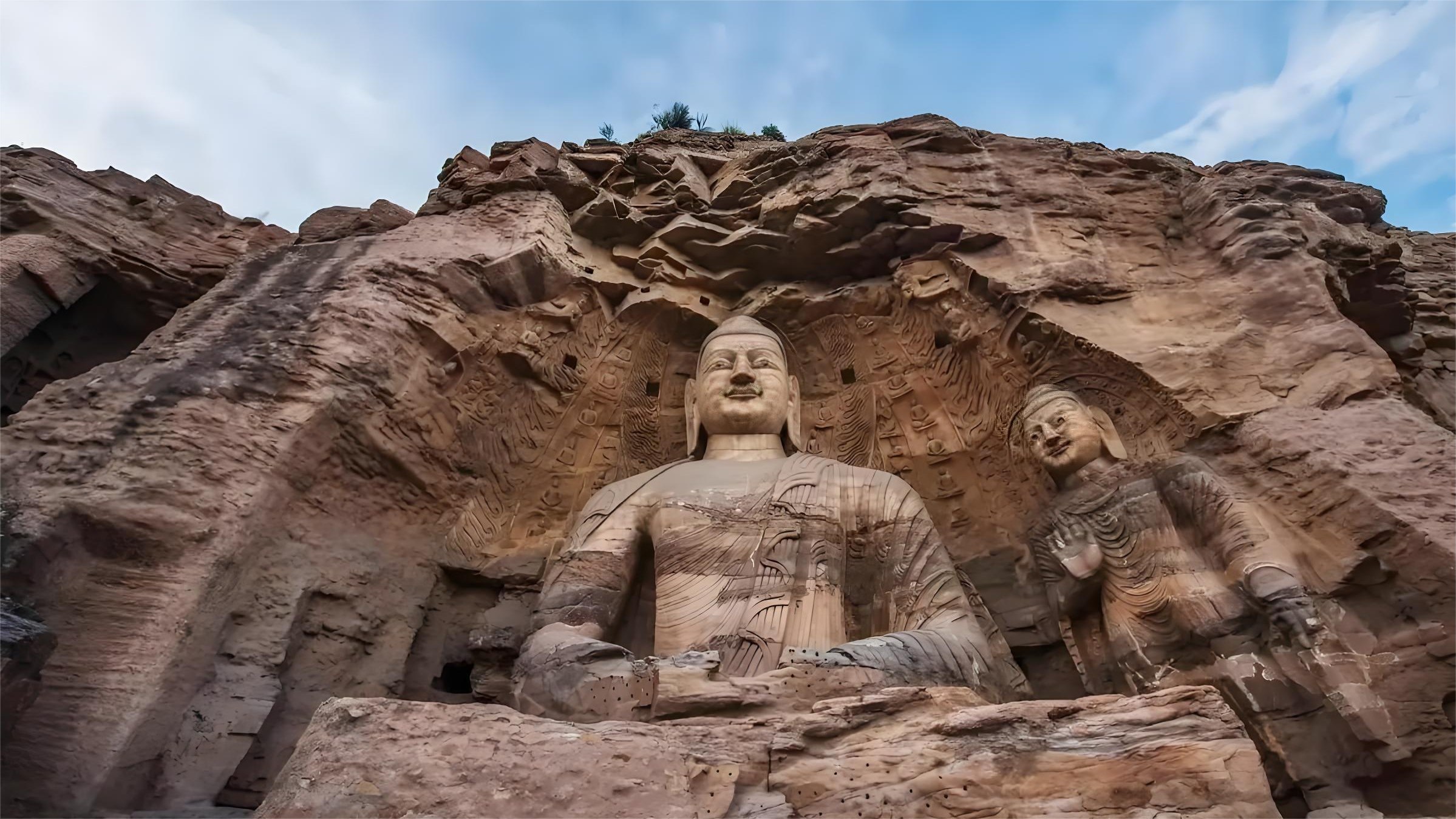 雲岡石窟的大佛,如第20窟露天坐佛,高達17米,面相方圓豐潤,鼻樑高挺,大耳垂肩,身著袒右肩式袈裟,展現出犍陀羅藝術與鮮卑審美的融合,是北魏佛教藝術中國化的重要象徵。 雲岡石窟的大佛,如第20窟露天坐佛,高達17米,面相方圓豐潤,鼻樑高挺,大耳垂肩,身著袒右肩式袈裟,展現出犍陀羅藝術與鮮卑審美的融合,是北魏佛教藝術中國化的重要象徵。