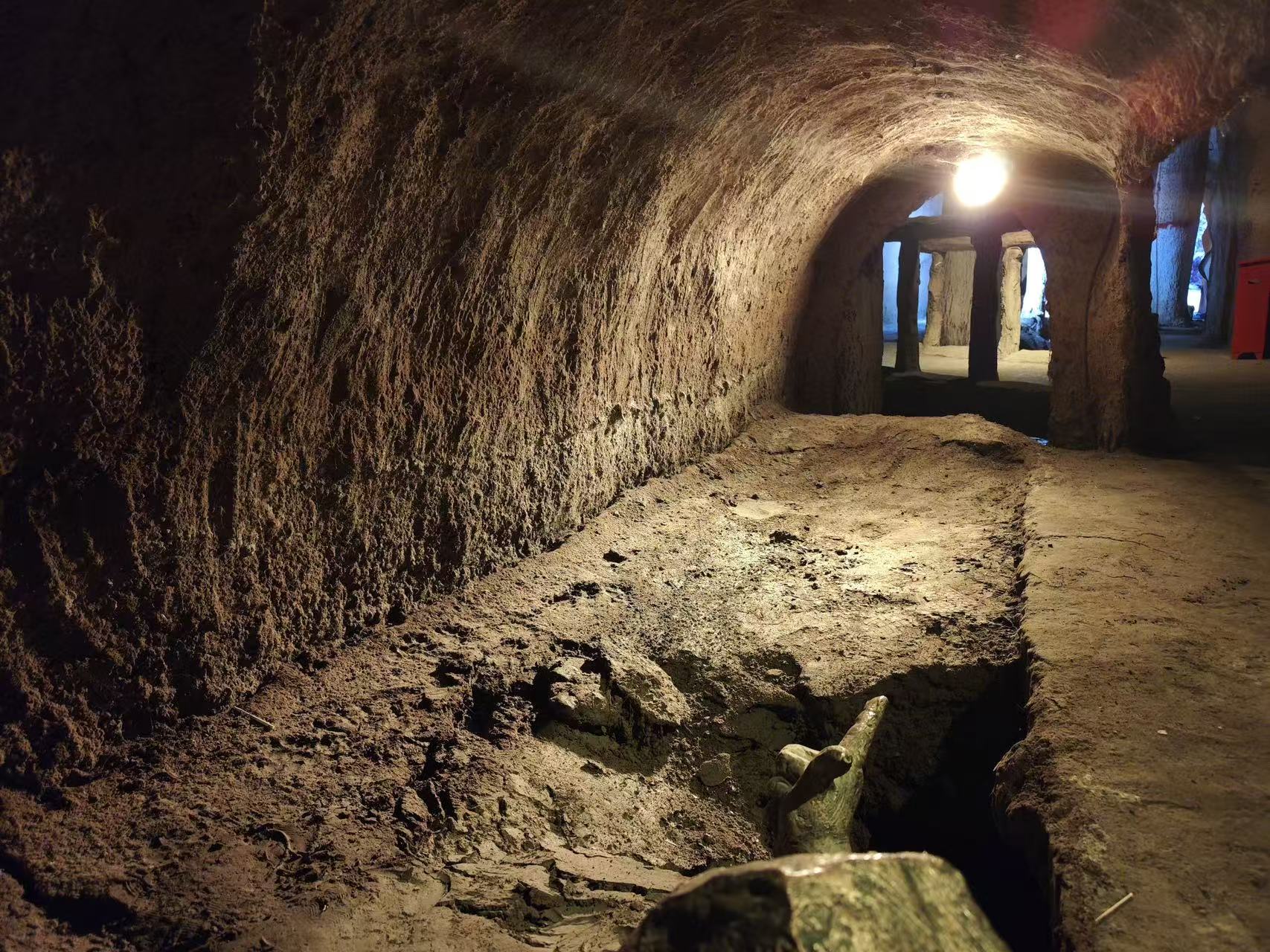 原生態土質拱形地下廊道,牆面與地面保留開鑿後的粗糙質感,暖光照明照亮通道,可見引水溝槽與勞作雕塑,直觀展現坎兒井地下輸水暗渠的原始樣貌 原生態土質拱形地下廊道,牆面與地面保留開鑿後的粗糙質感,暖光照明照亮通道,可見引水溝槽與勞作雕塑,直觀展現坎兒井地下輸水暗渠的原始樣貌