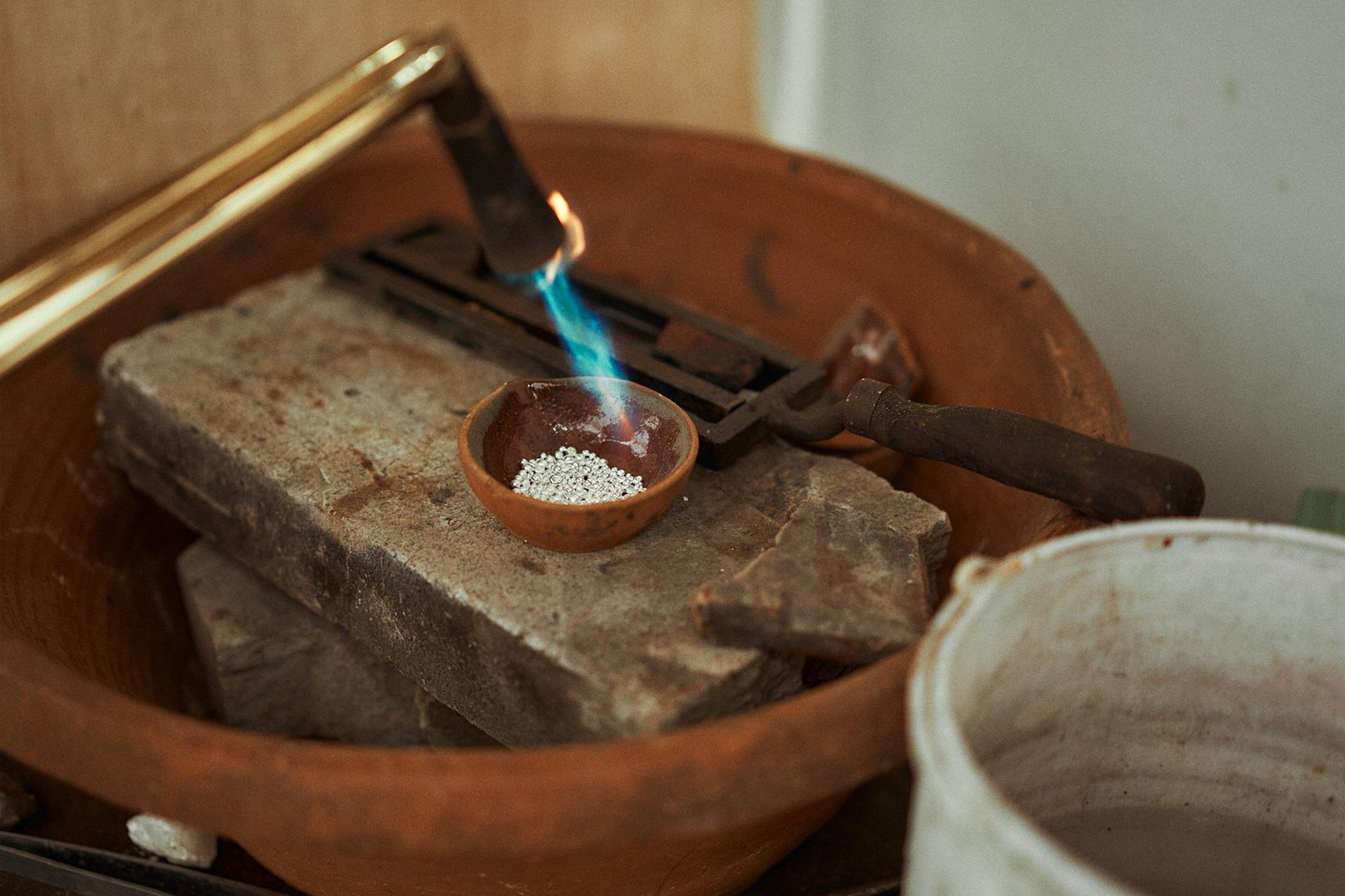 Silver beads are being heated with a blue flame, the initial stage of the jewelry making process which requires great precision.