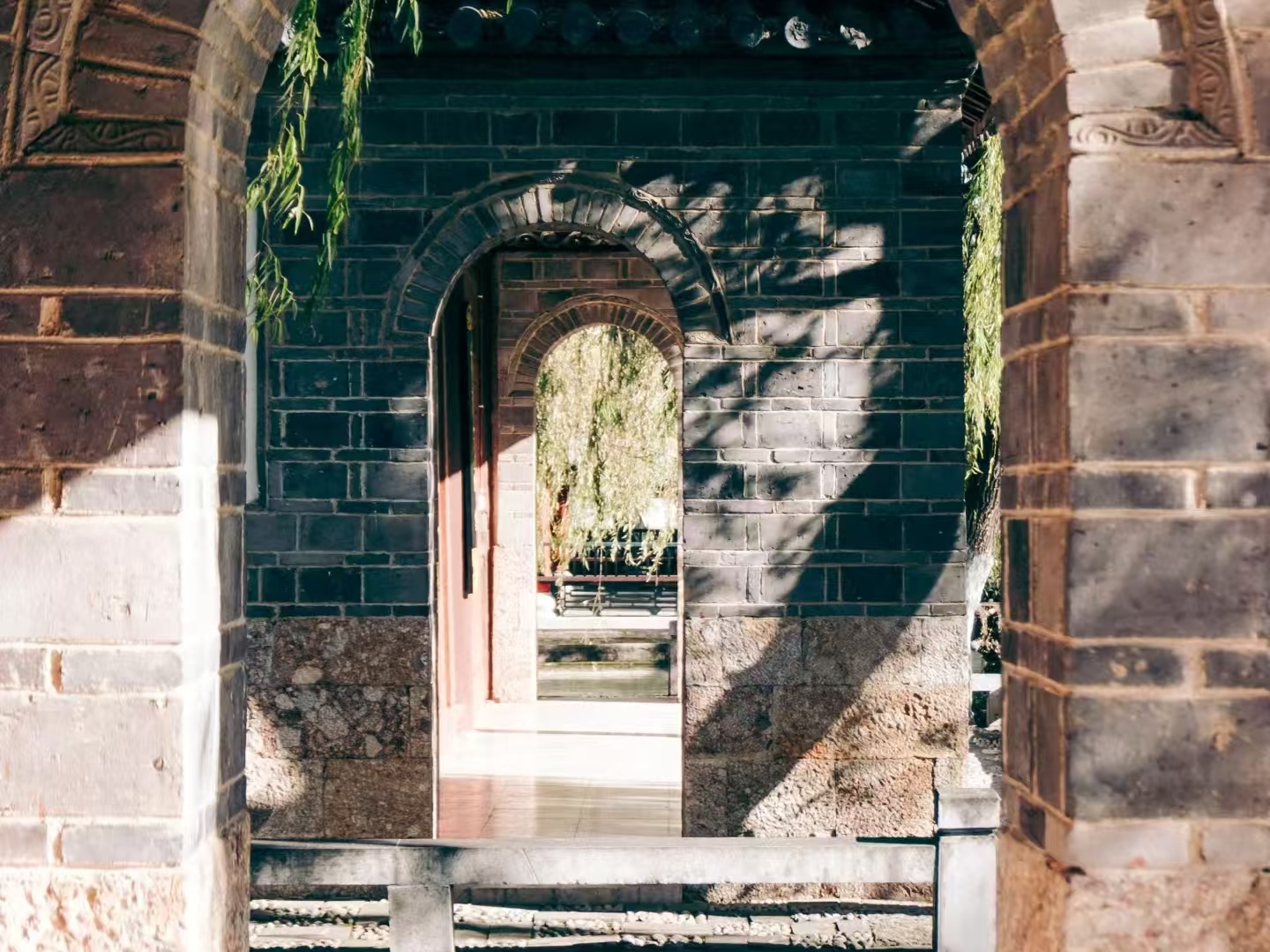 光影在牆面勾勒出斑駁紋路，透過拱門可見庭院水景，盡顯木府空間的層次與靜謐之美