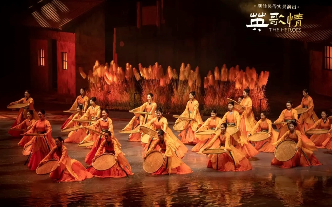 眾多演員身著橙紅漸變服飾,手持竹笠在水間起舞。背景的 “蘆葦” 與古建呼應,營造出濃郁潮汕水鄉氛圍,以整齊劃一的舞蹈,展現民俗文化的群體性與感染力,訴說潮汕風土人情 眾多演員身著橙紅漸變服飾,手持竹笠在水間起舞。背景的 “蘆葦” 與古建呼應,營造出濃郁潮汕水鄉氛圍,以整齊劃一的舞蹈,展現民俗文化的群體性與感染力,訴說潮汕風土人情