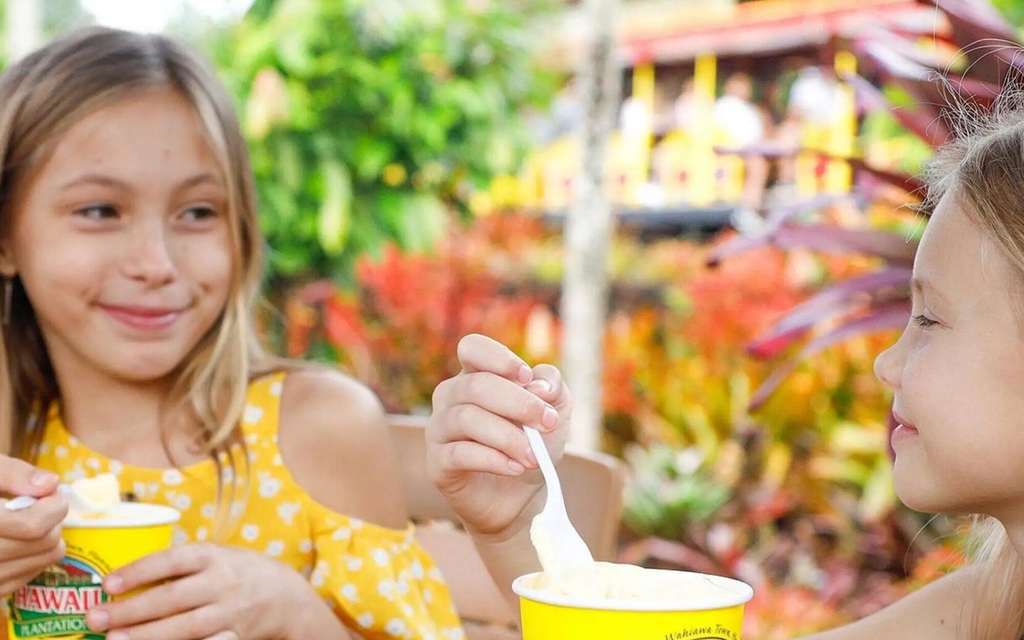 孩童們在歐胡島都樂鳳梨園的戶外，背景是熱帶植物和繽紛的環境，享受著鳳梨甜點。
