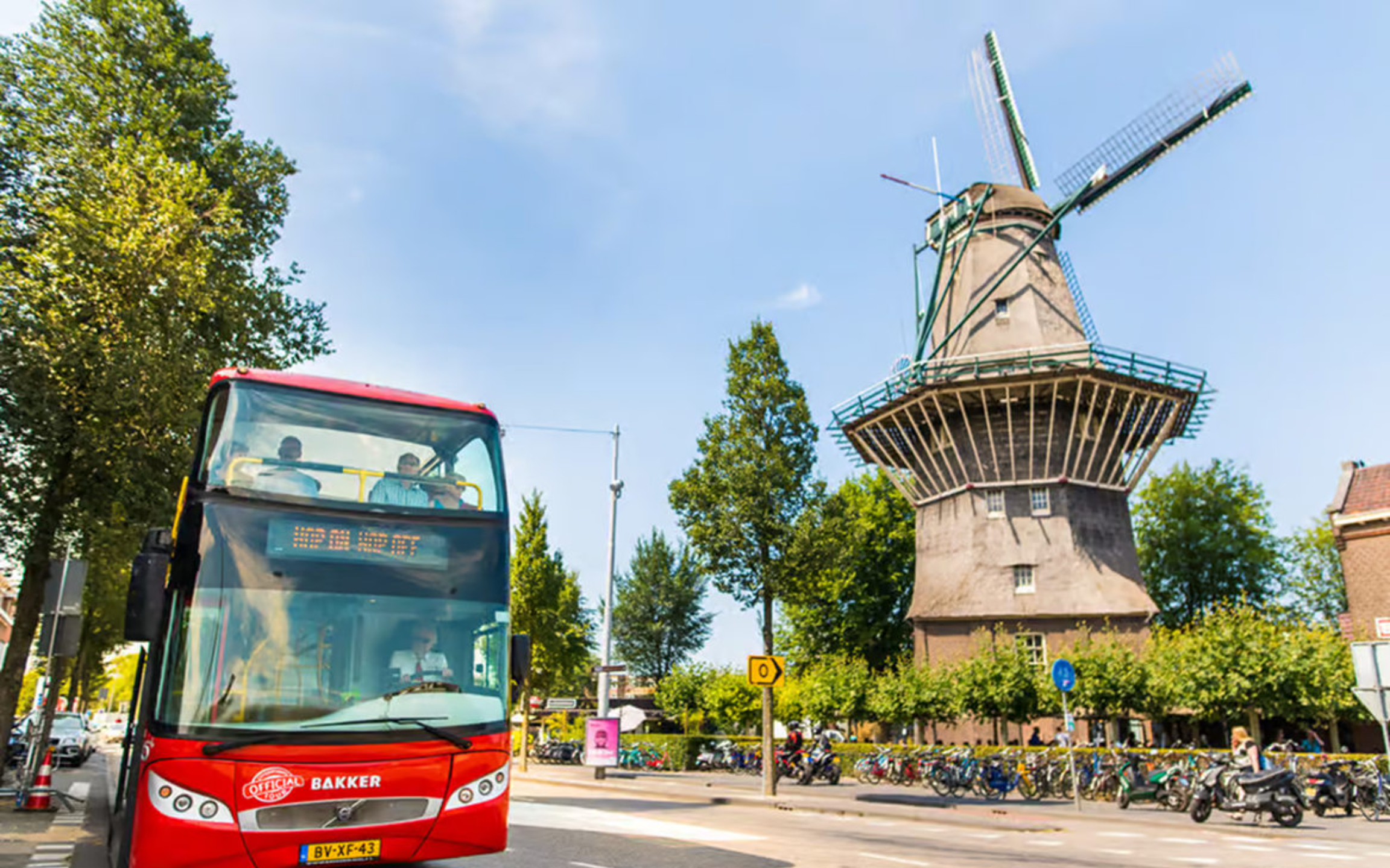 A city sightseeing bus parked beside a Dutch windmill structure, showcasing iconic local culture and scenery
