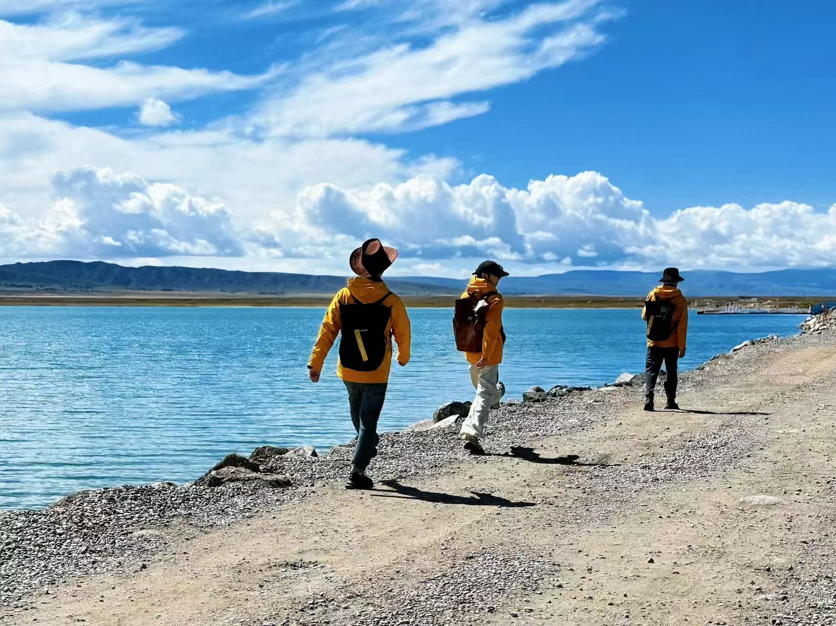 澄澈青海湖與遠山白雲作背景,三位同穿黃外套的遊客沿碎石湖岸漫步,揹包帽子各有特色,人影落在路面。畫面鬆弛自然,生動還原結伴環湖慢行、悠閒出遊的旅途瞬間 澄澈青海湖與遠山白雲作背景,三位同穿黃外套的遊客沿碎石湖岸漫步,揹包帽子各有特色,人影落在路面。畫面鬆弛自然,生動還原結伴環湖慢行、悠閒出遊的旅途瞬間