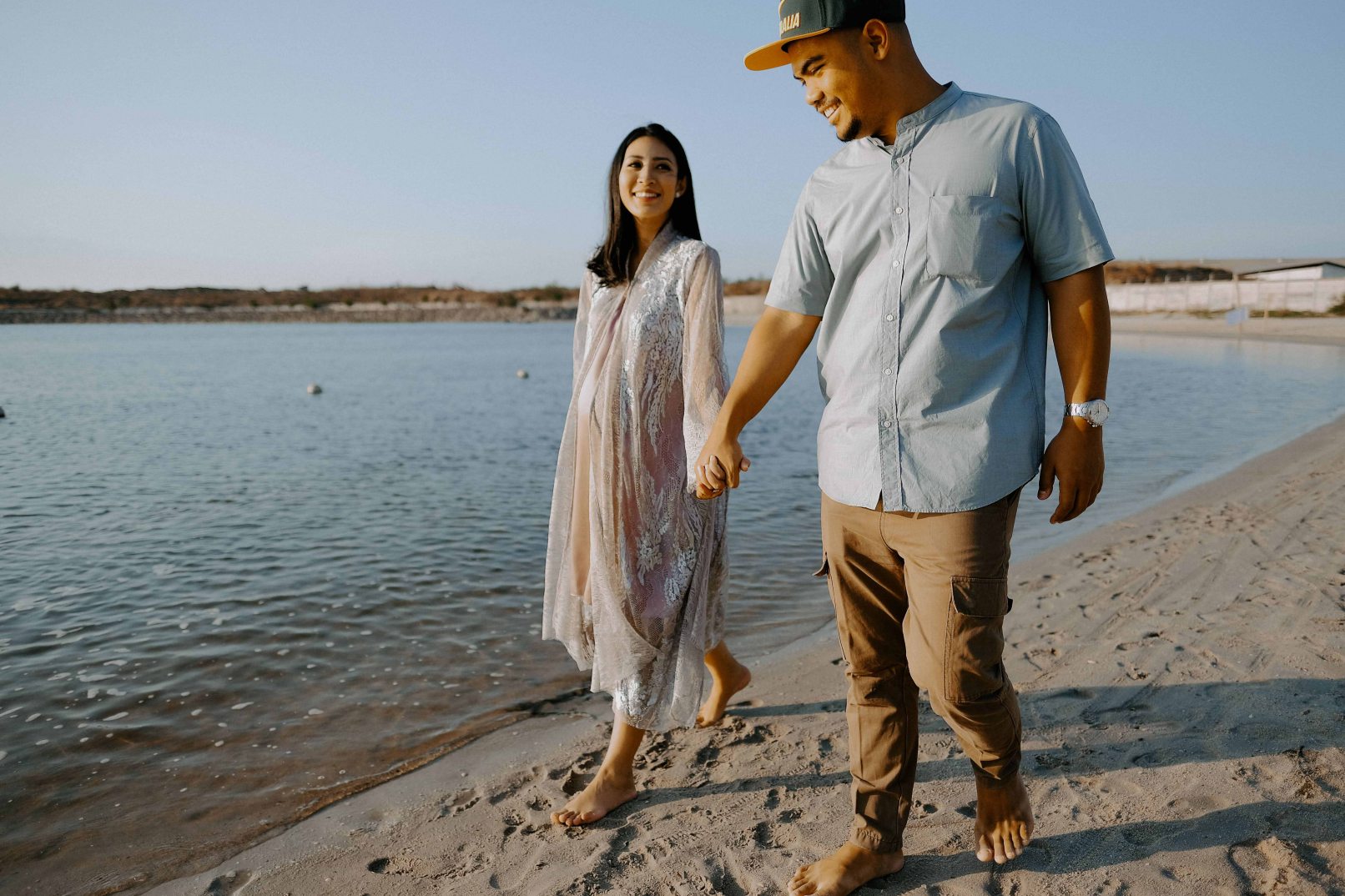 Man and woman holding hands while walking on beach