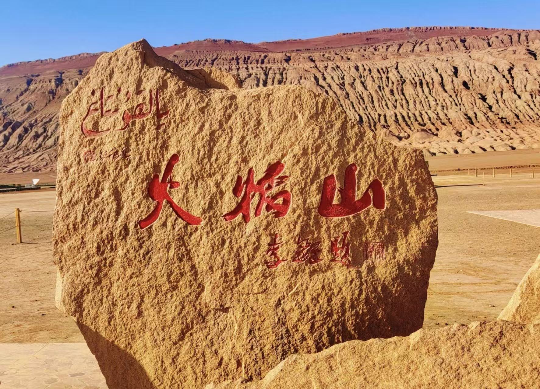淺黃岩石石碑刻有鮮紅 “火焰山” 大字,附題字與維吾爾文,背景是溝壑縱橫的紅褐色山體,荒漠曠野開闊遼遠,是火焰山景區經典打卡標識點位 淺黃岩石石碑刻有鮮紅 “火焰山” 大字,附題字與維吾爾文,背景是溝壑縱橫的紅褐色山體,荒漠曠野開闊遼遠,是火焰山景區經典打卡標識點位