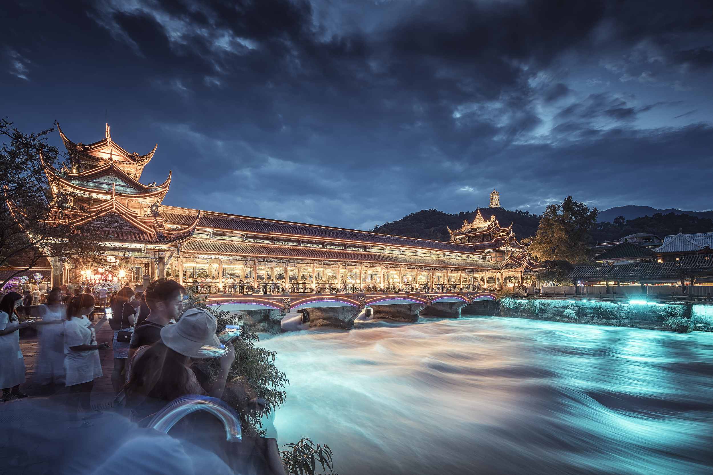 都江堰南橋，一座矗立在岷江之上的千年古橋，如一顆璀璨明珠閃耀在都江堰景區。
橋身雕樑畫棟，飛簷翹角，琉璃瓦熠熠生輝，精美的彩繪、彩塑、書畫融為一體，構成了一座美輪美奐的“水上畫樓”，漫步其間，彷彿置身於藝術殿堂。
當夜幕降臨，南橋更是換上夢幻華服，“藍眼淚”景觀如夢似幻，燈光映照下，岷江水宛如藍色眼淚傾瀉，與古橋交相輝映，形成一幅絕美的光影畫卷。