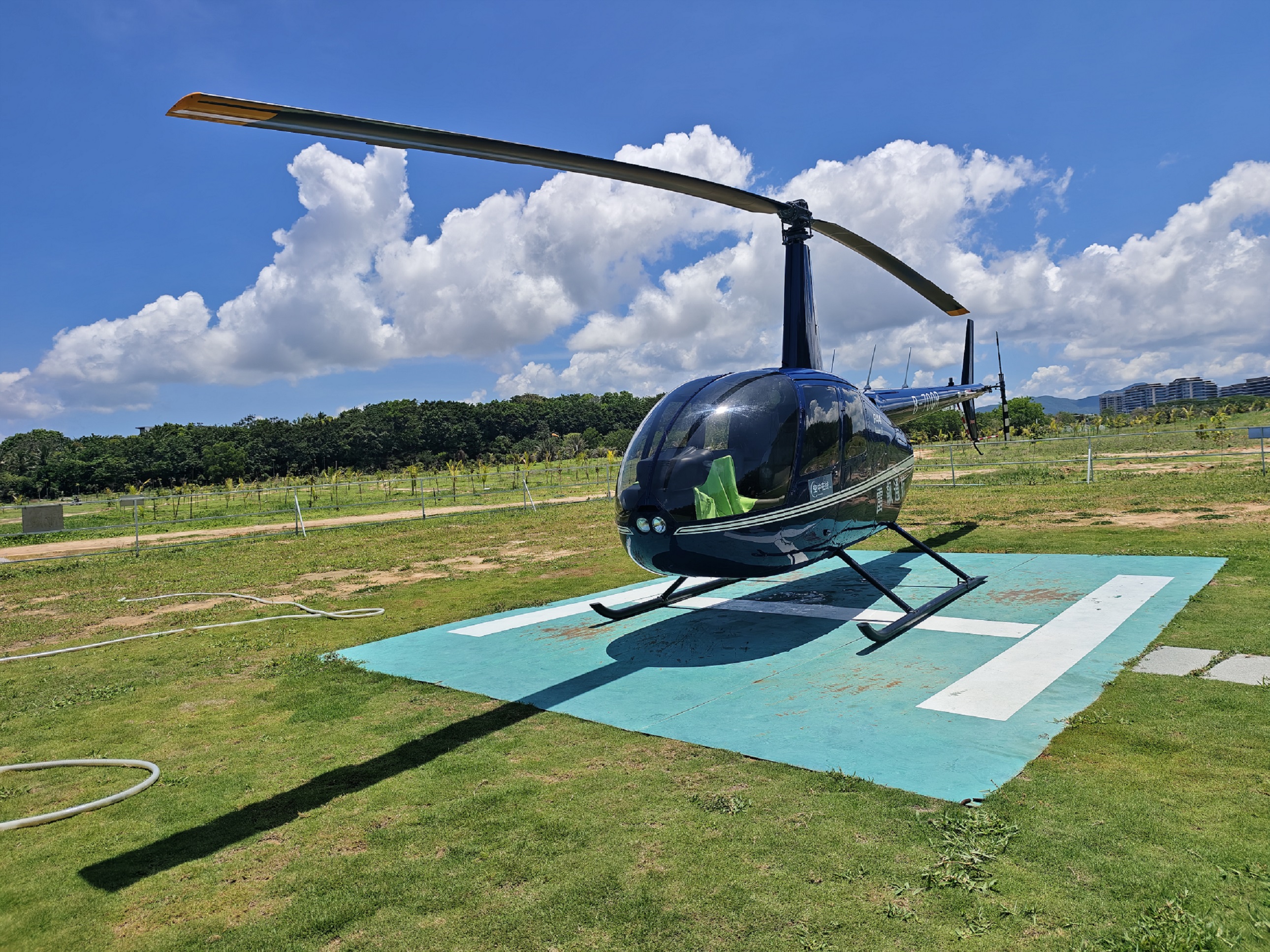 深藍直升機的機身映著身後亞特蘭蒂斯飯店的流線型尖頂，玻璃幕牆與棕櫚葉在陽光下織成明暗交錯的網